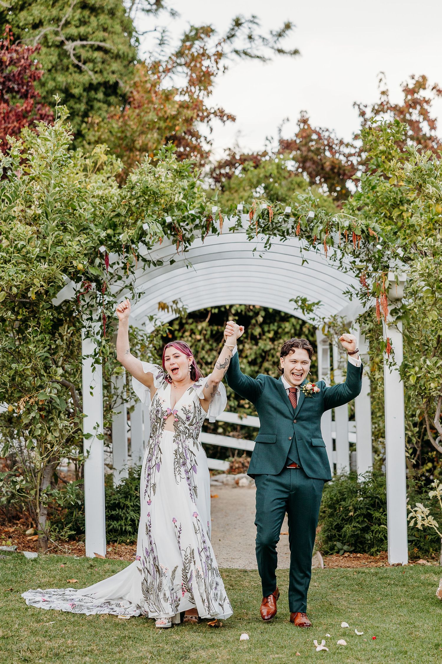 Joyful wedding celebration under a white garden arbor with people raising their arms in celebration.