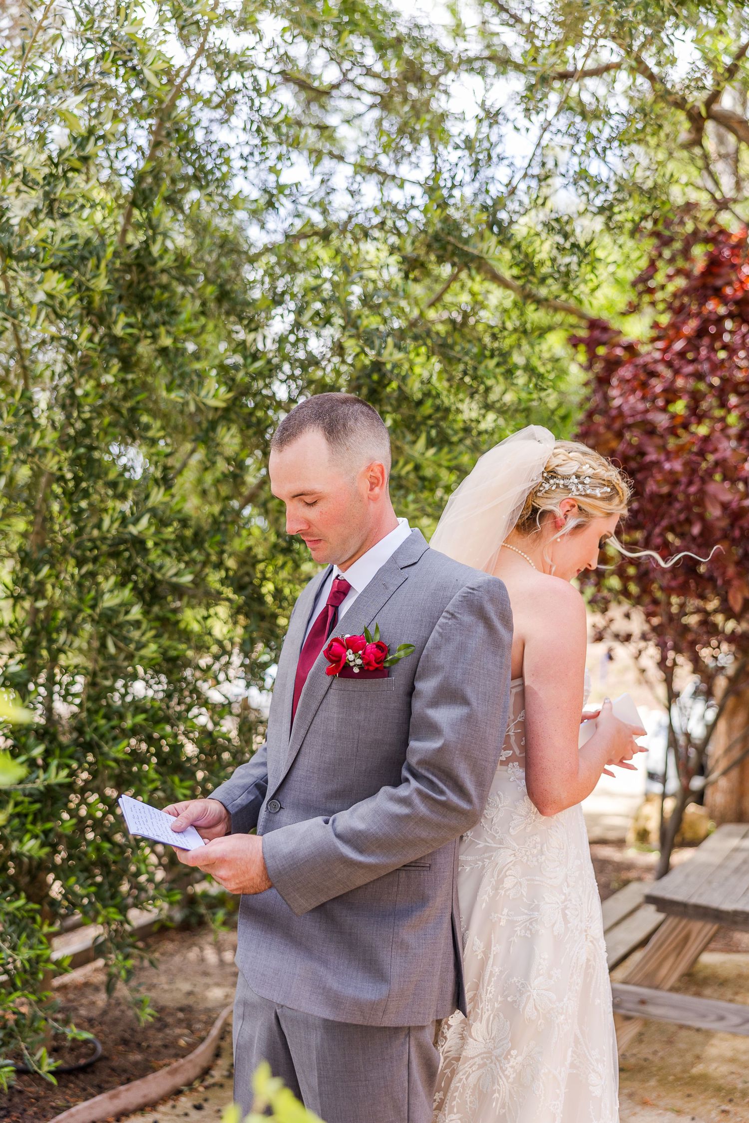 Couple shares private moment reading letters during first look in lush garden setting.