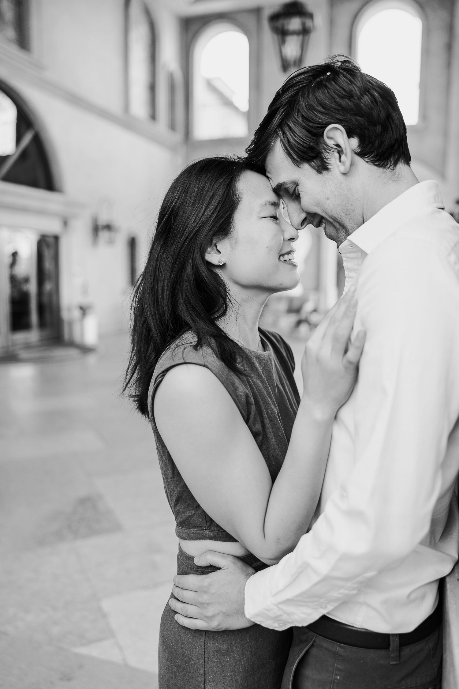 A romantic black and white portrait of a couple sharing an intimate moment in an arched hallway.