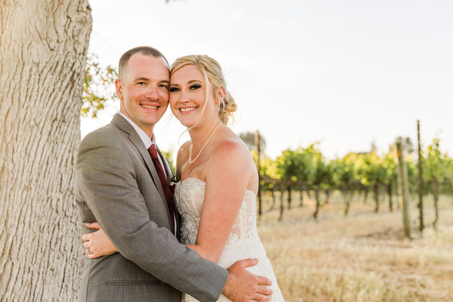 A couple embracing in front of a vineyard wearing wedding attire.