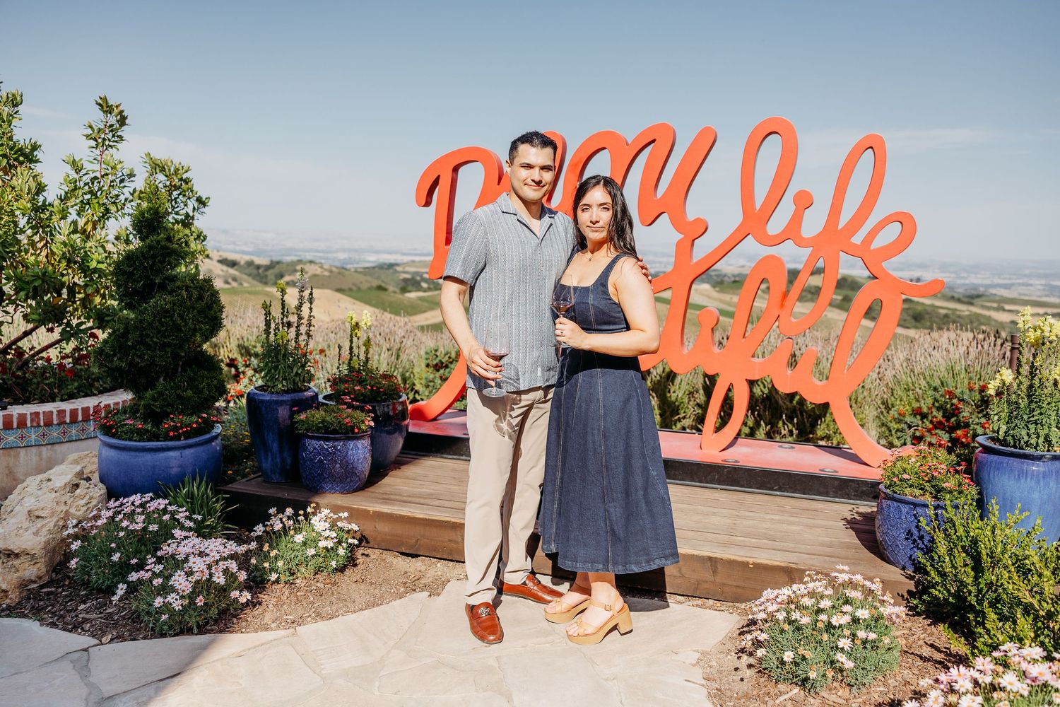 A couple poses together on a scenic terrace with mountain views and decorative signage.