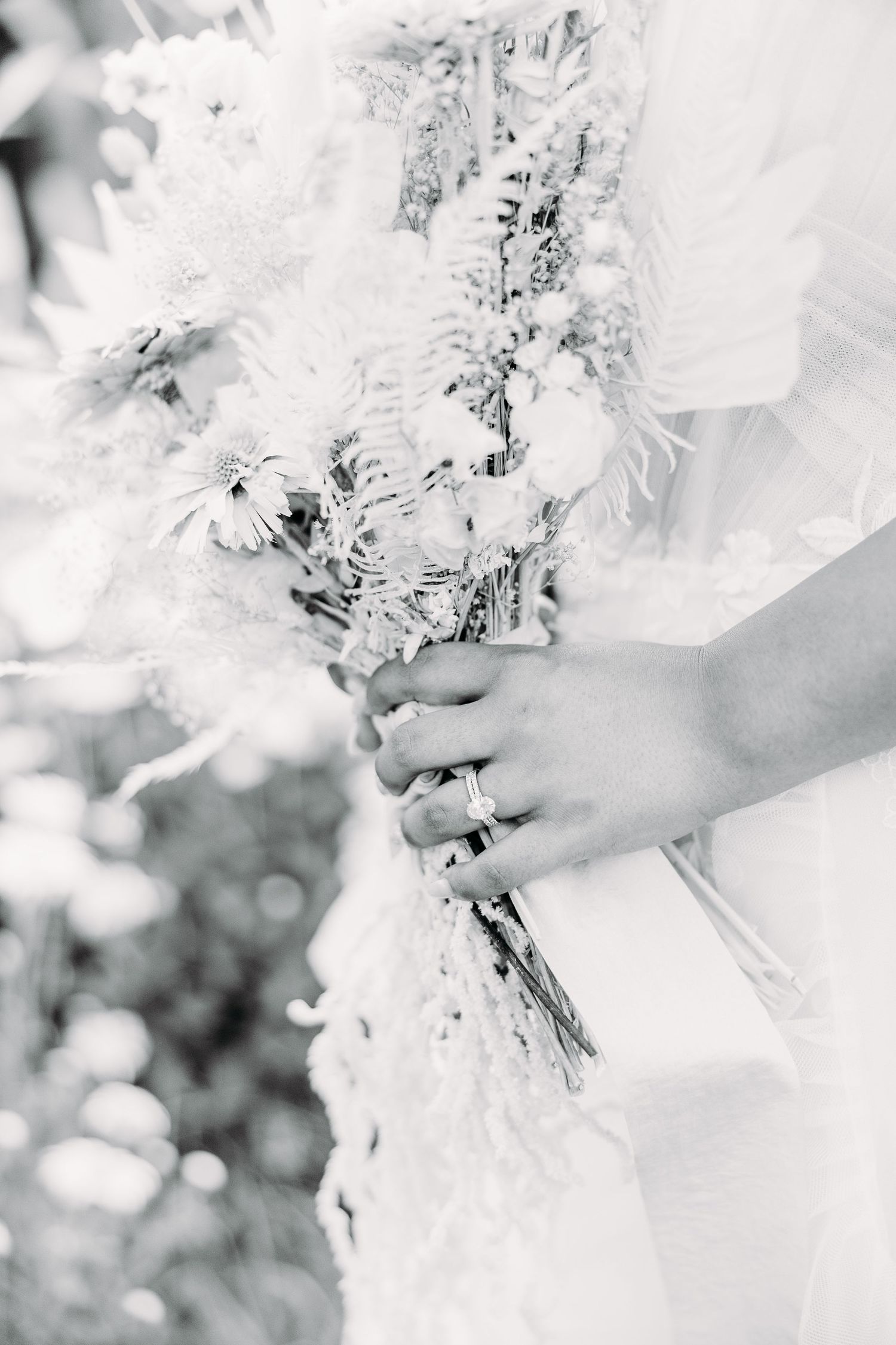 Black and white close-up of hands holding delicate dried flower wedding bouquet.