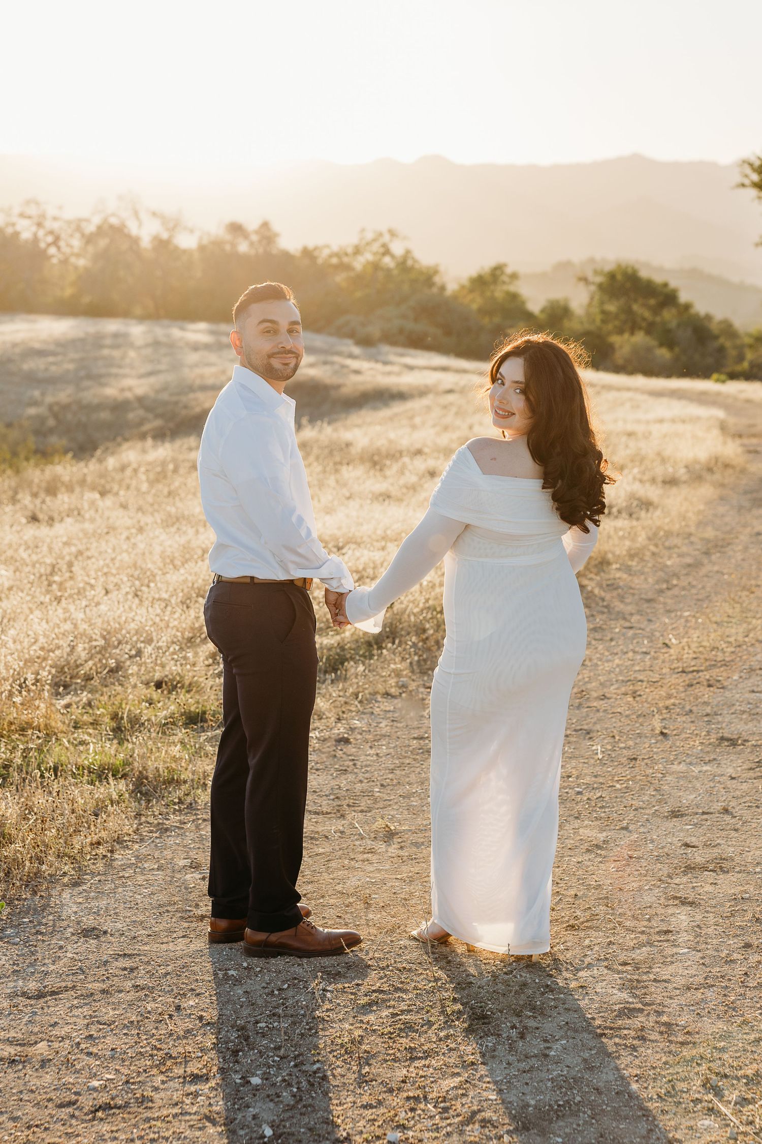 Couple in contrasting outfits share playful moments on a sun-drenched hiking trail.