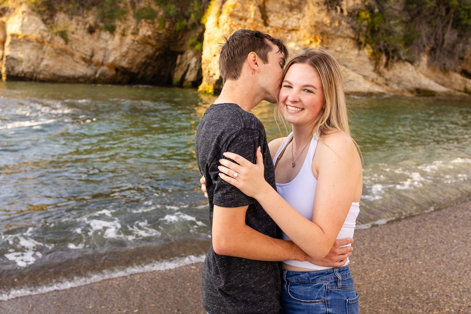 A romantic moment captured between a couple laughing together on a pebble beach.
