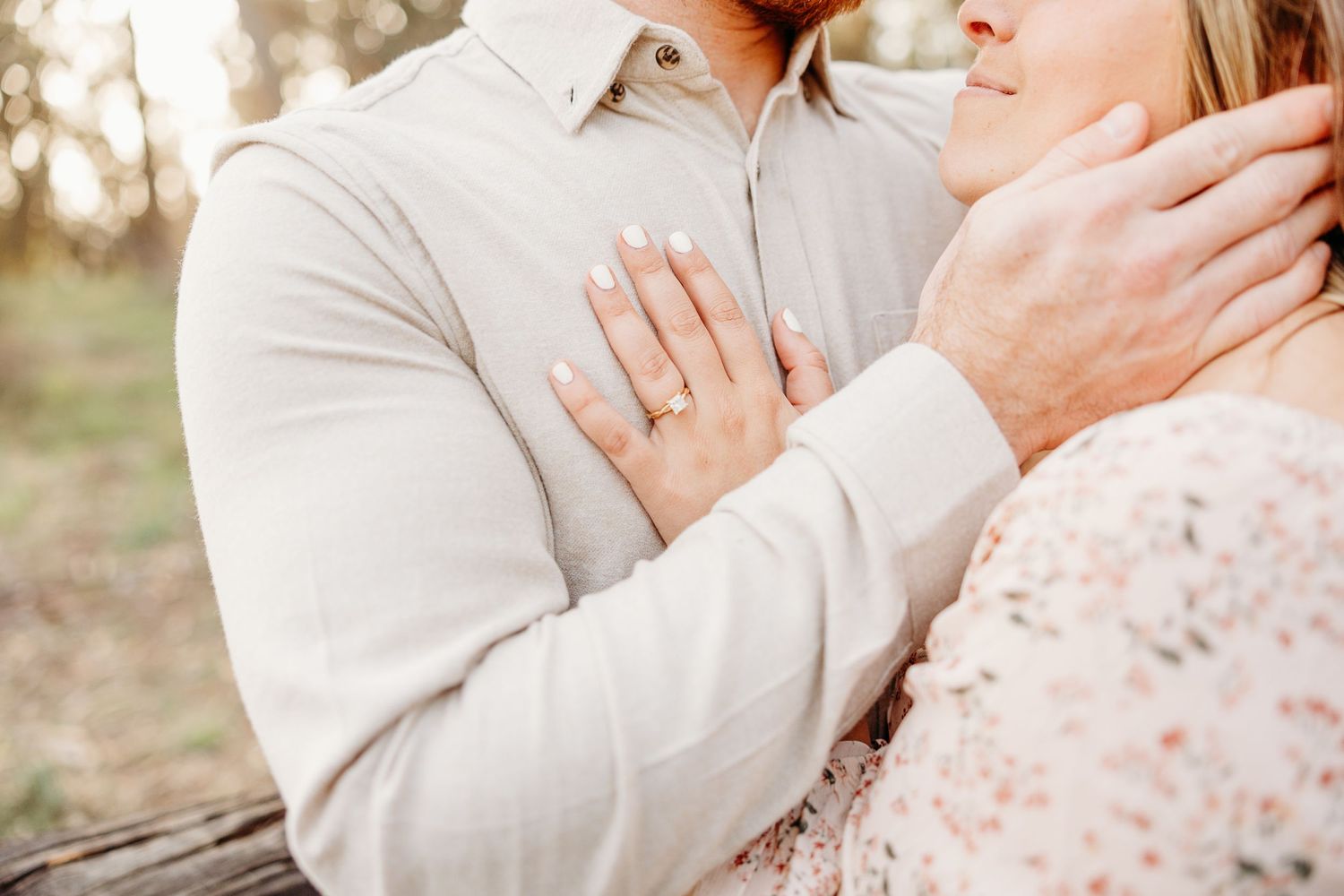 Close up of couple's embrace showing engagement ring in golden sunlight.