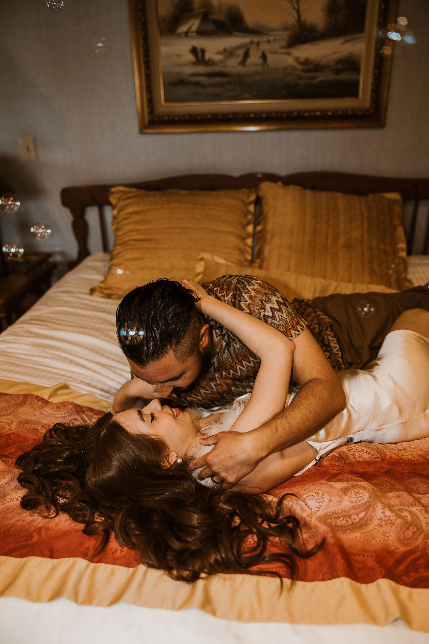 Romantic couple sharing an intimate moment on a bed with golden pillows and vintage decor in warm lighting.