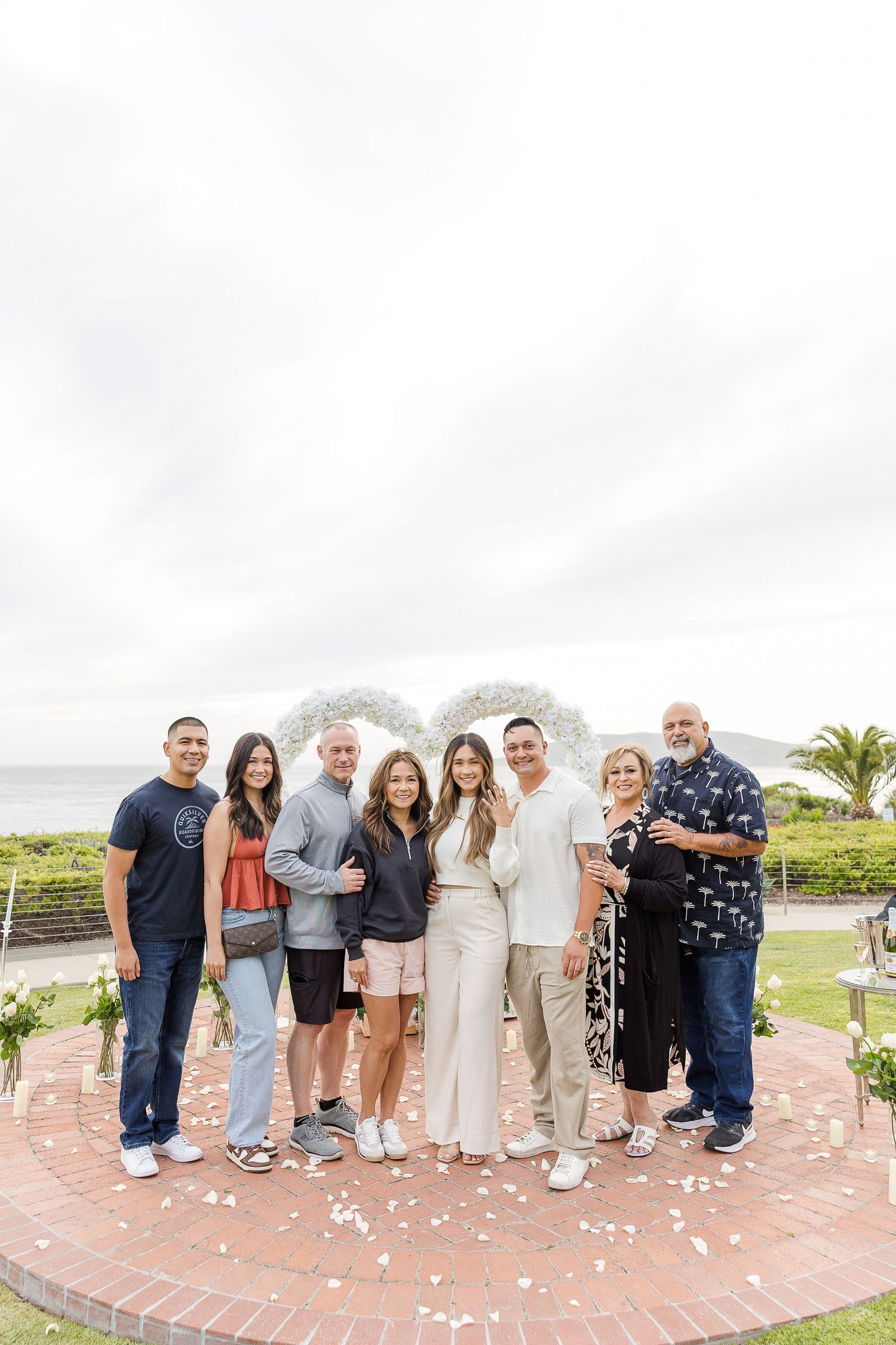A large group of people lined up for a wedding photo on a pink brick patio with palm trees in the background.