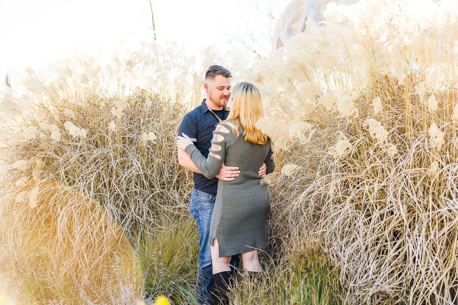 A romantic couple embraces among tall golden grass during a sunset photo session.