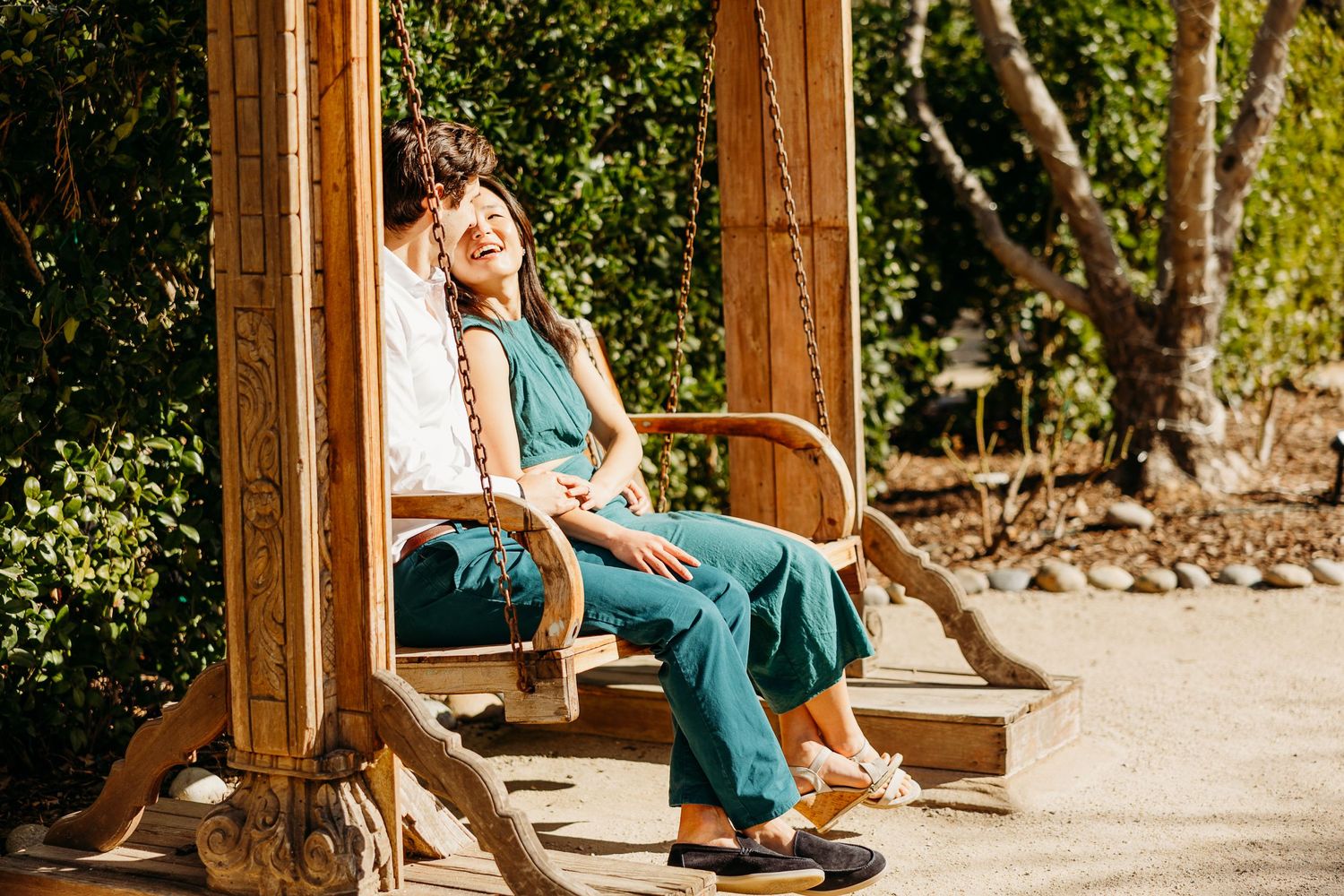A couple sharing a tender moment while sitting on a wooden swing in a garden.