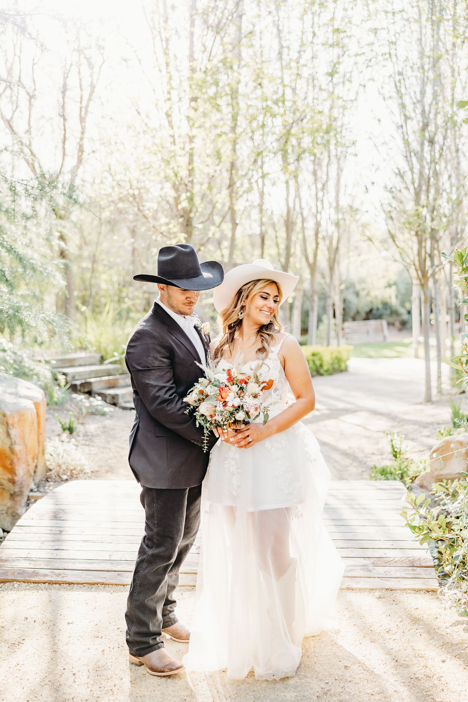 A Western-style wedding couple poses on a wooden walkway surrounded by trees and natural scenery.