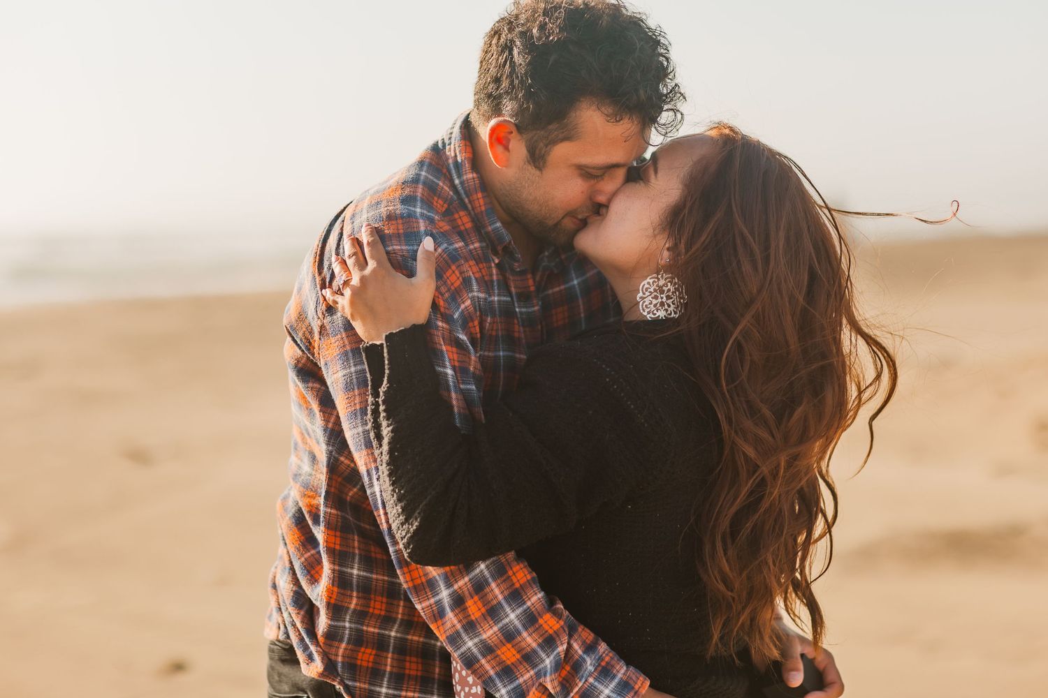 A romantic embrace on a sandy beach during golden hour.