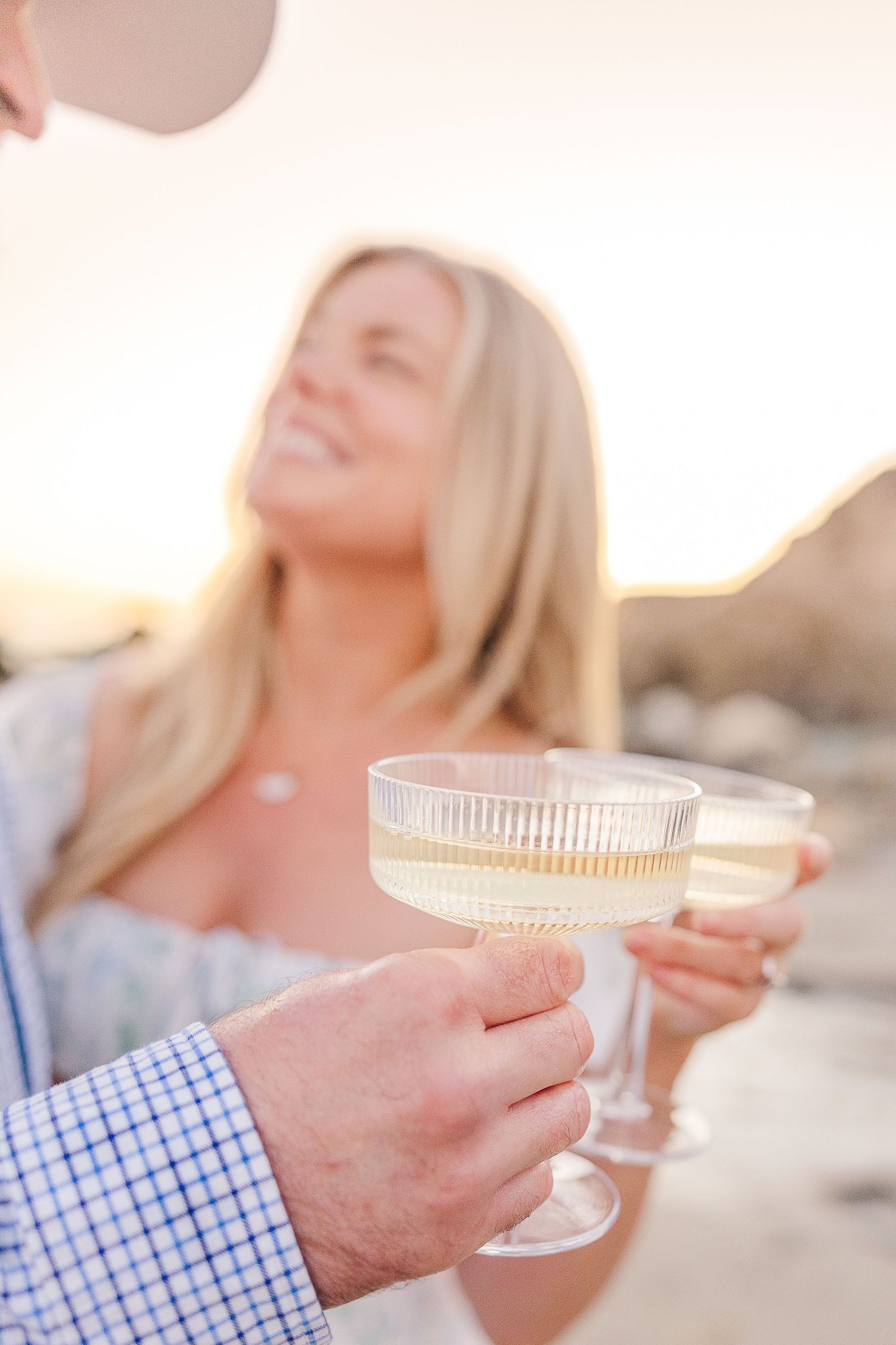 Two champagne glasses clink together against a warm sunset backdrop at the beach.
