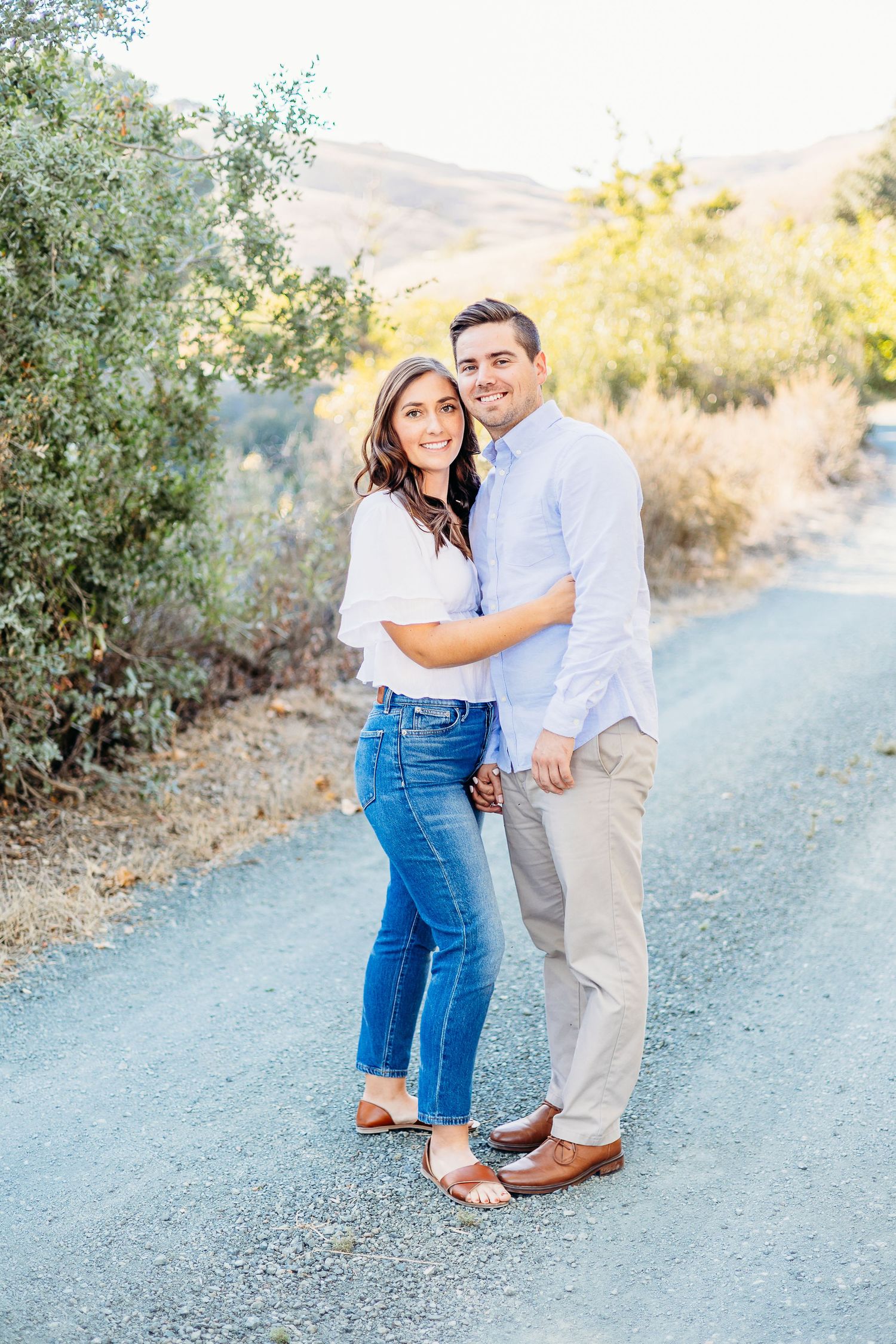 A couple posing together on a dirt path with mountains in the background.