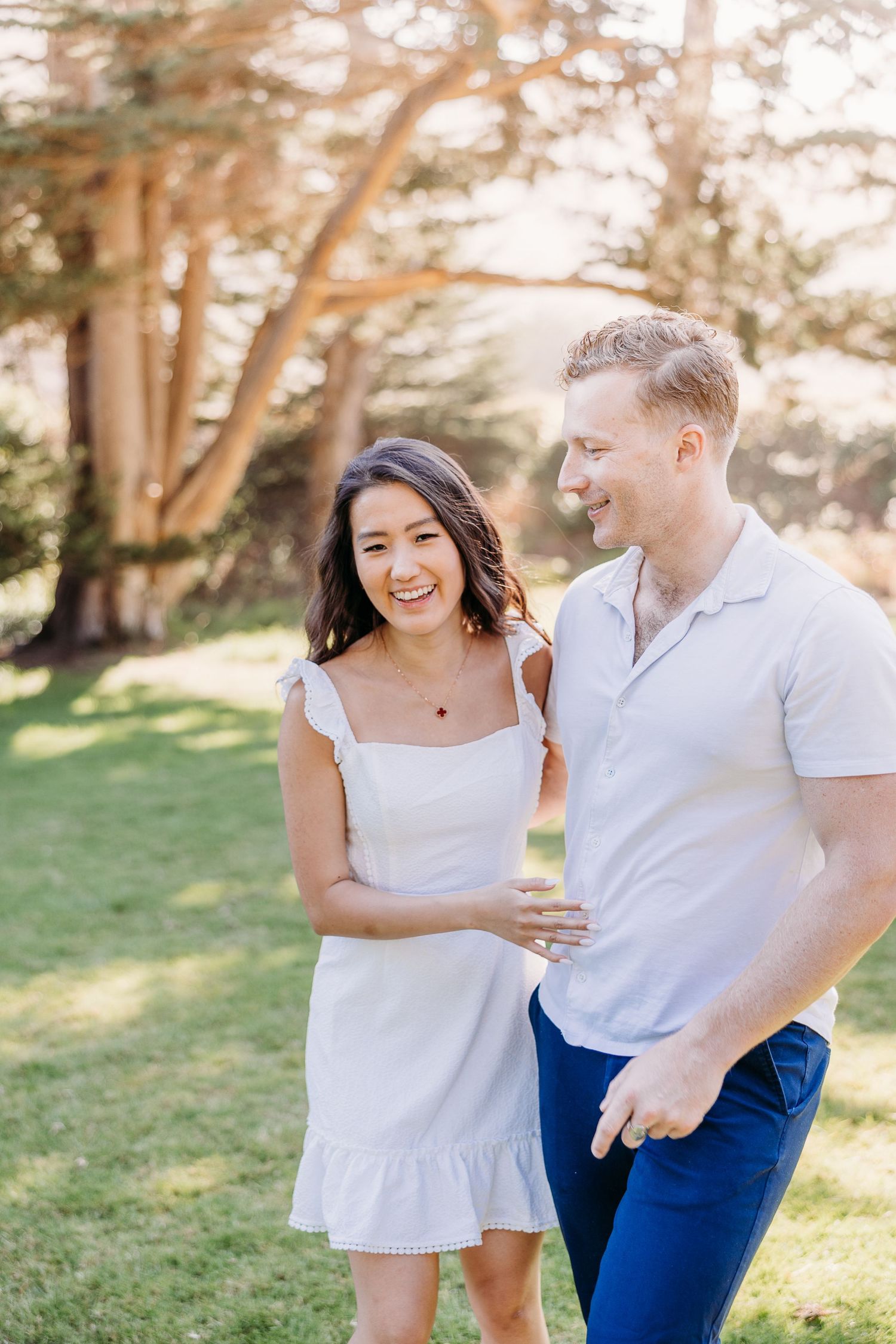 A happy couple shares laughter while walking together in a park on a bright summer day.