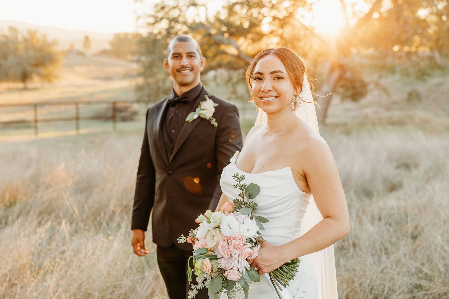 Joyful wedding couple embracing during golden hour photography session in rustic outdoor setting.