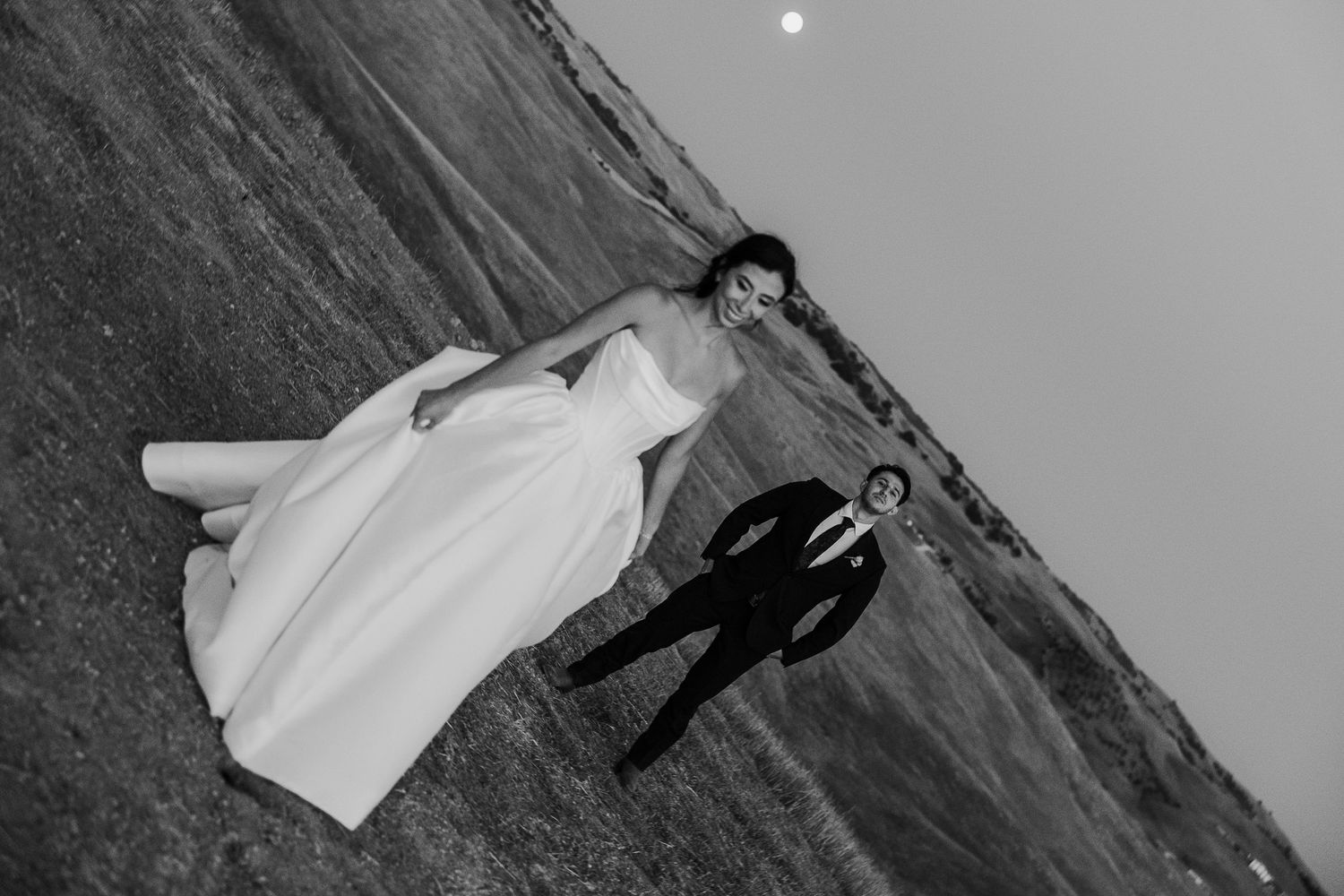 Artistic black and white wedding portrait on hillside with full moon.