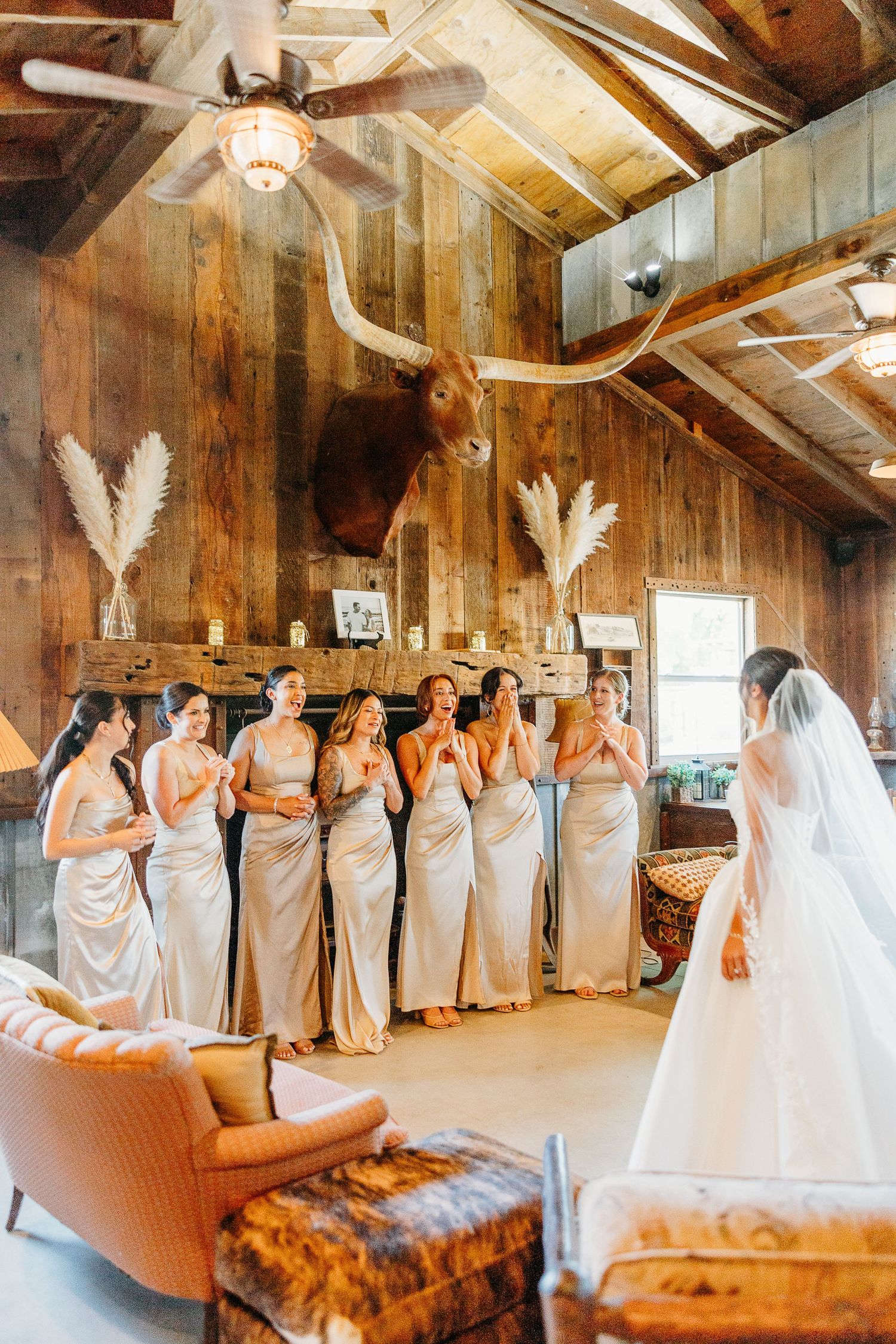 Bridesmaids in champagne dresses line up in a rustic barn venue during a wedding celebration.