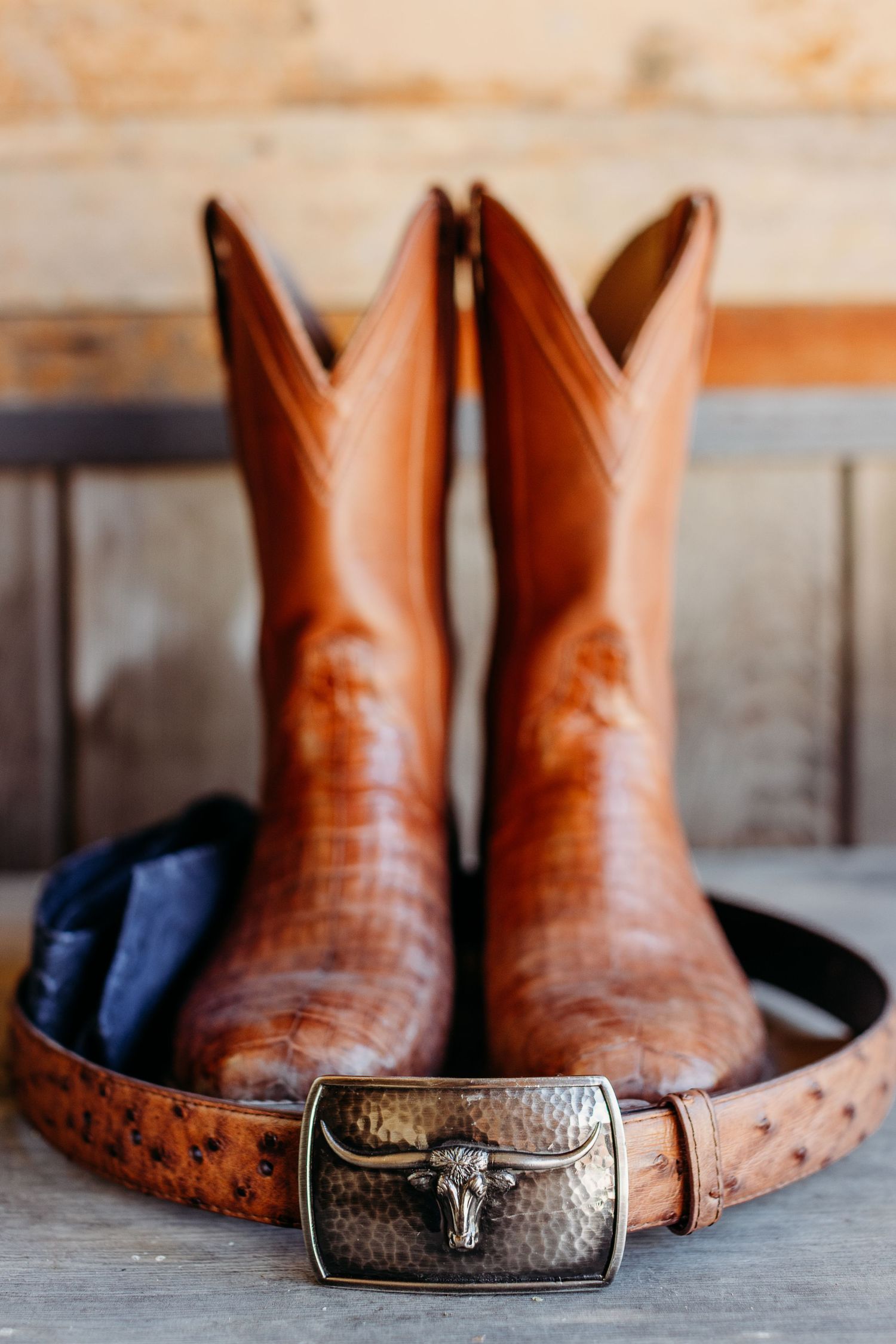 Brown leather cowboy boots and a western belt with longhorn buckle arranged on wooden surface.