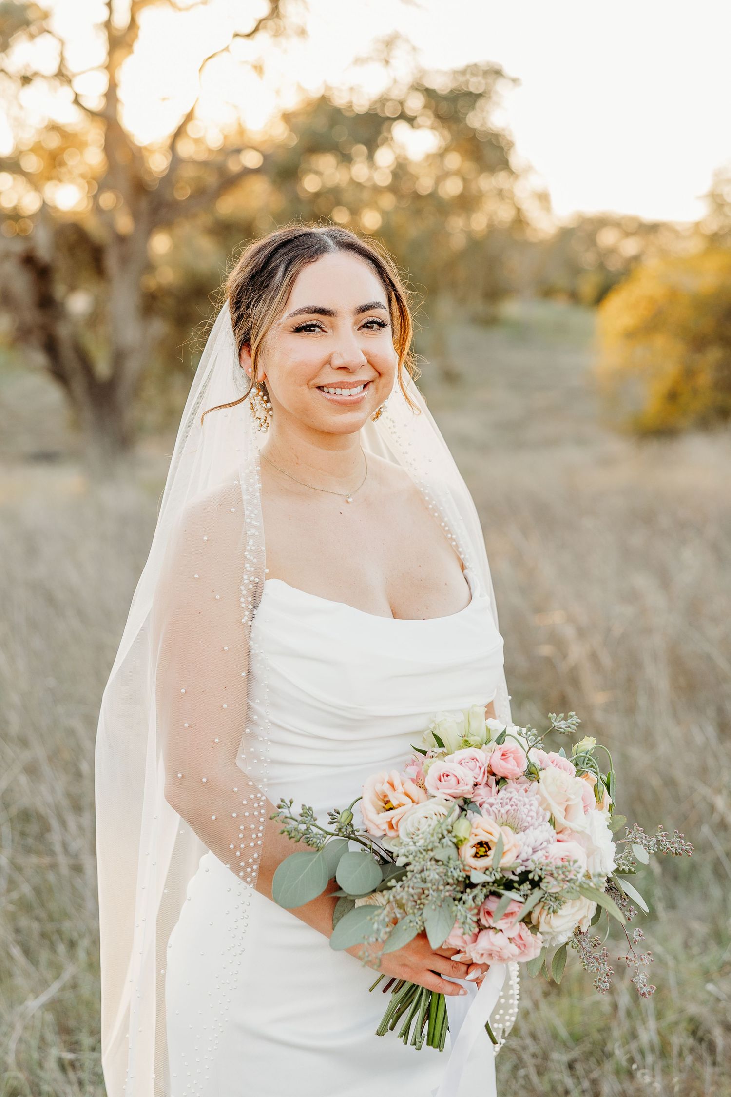 Bride holding a beautiful bouquet of pink and white flowers with greenery in natural outdoor setting.