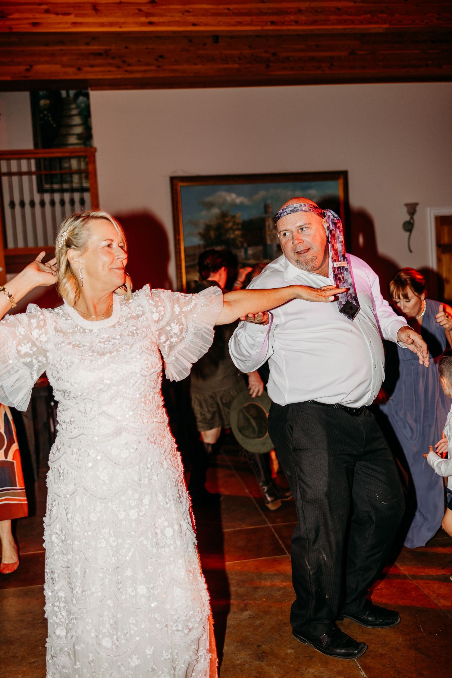 Wedding reception guests dancing energetically on indoor dance floor.