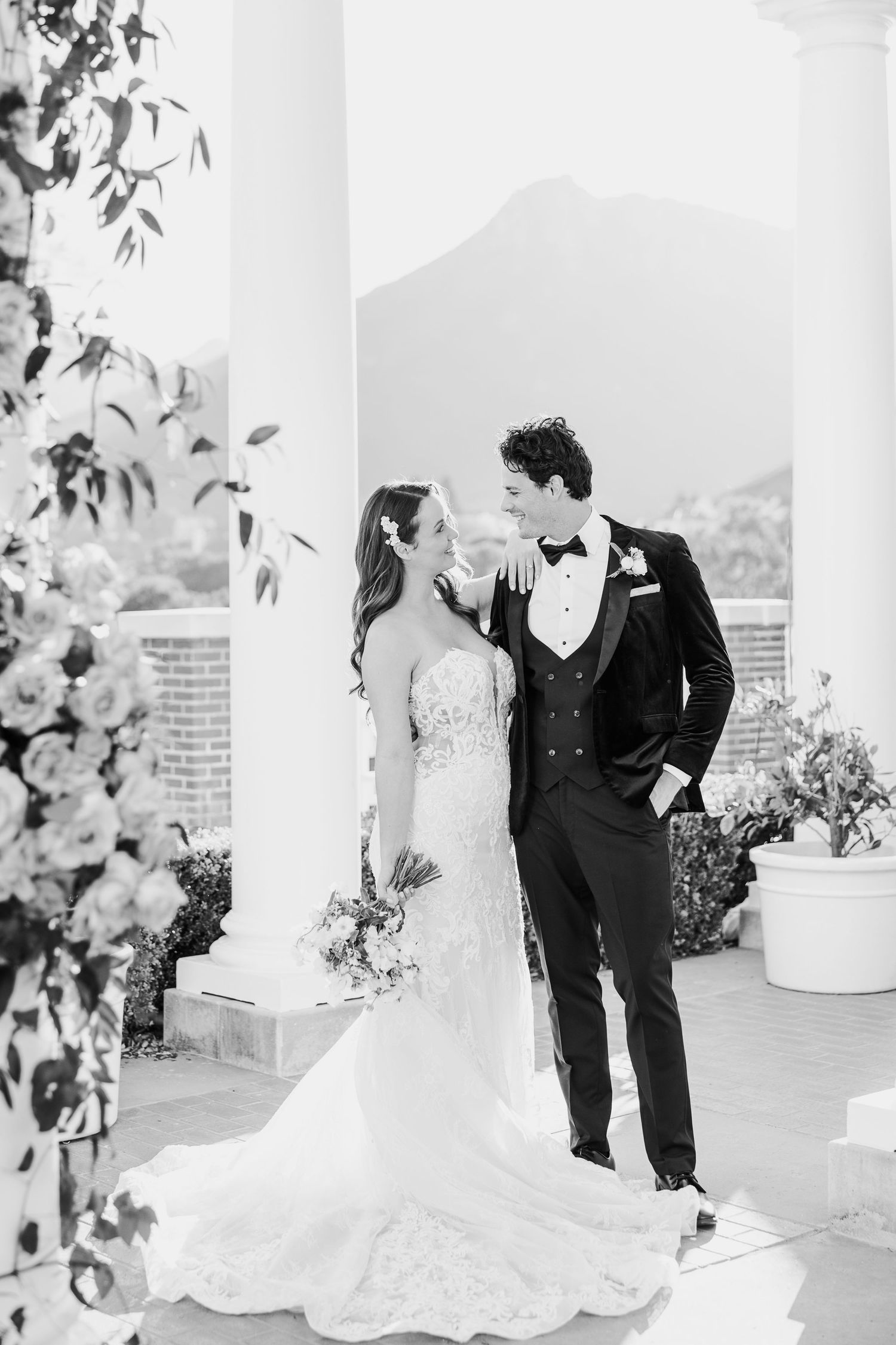 Elegant wedding couple shares a romantic moment between white columns on their special day.