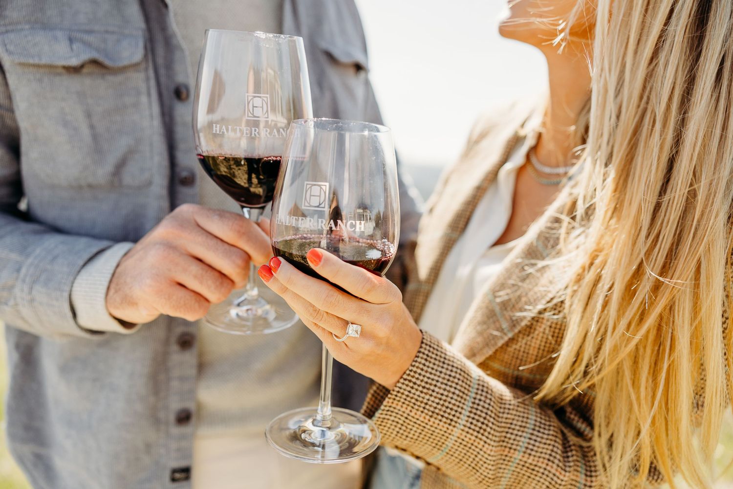 Two people toasting with glasses of red wine in sunlight while wearing casual attire.