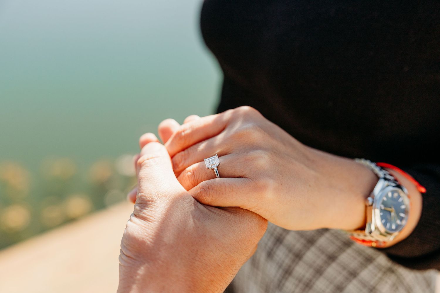 Close-up of hands exchanging an engagement ring during a proposal in natural outdoor lighting.