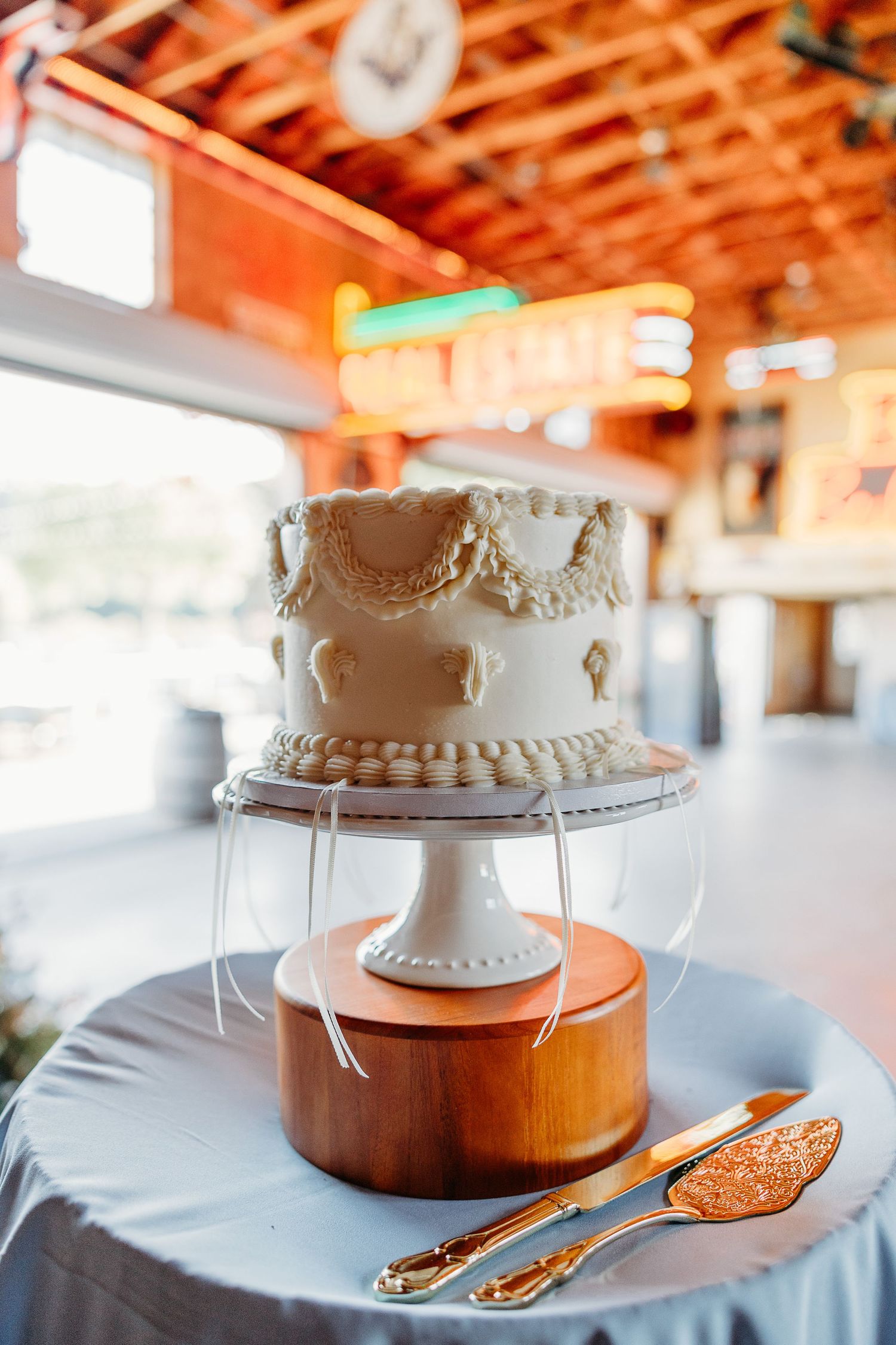 An elegant white wedding cake displayed on a wooden stand with decorative serving utensils in local wedding venue Holland Ranch SLO