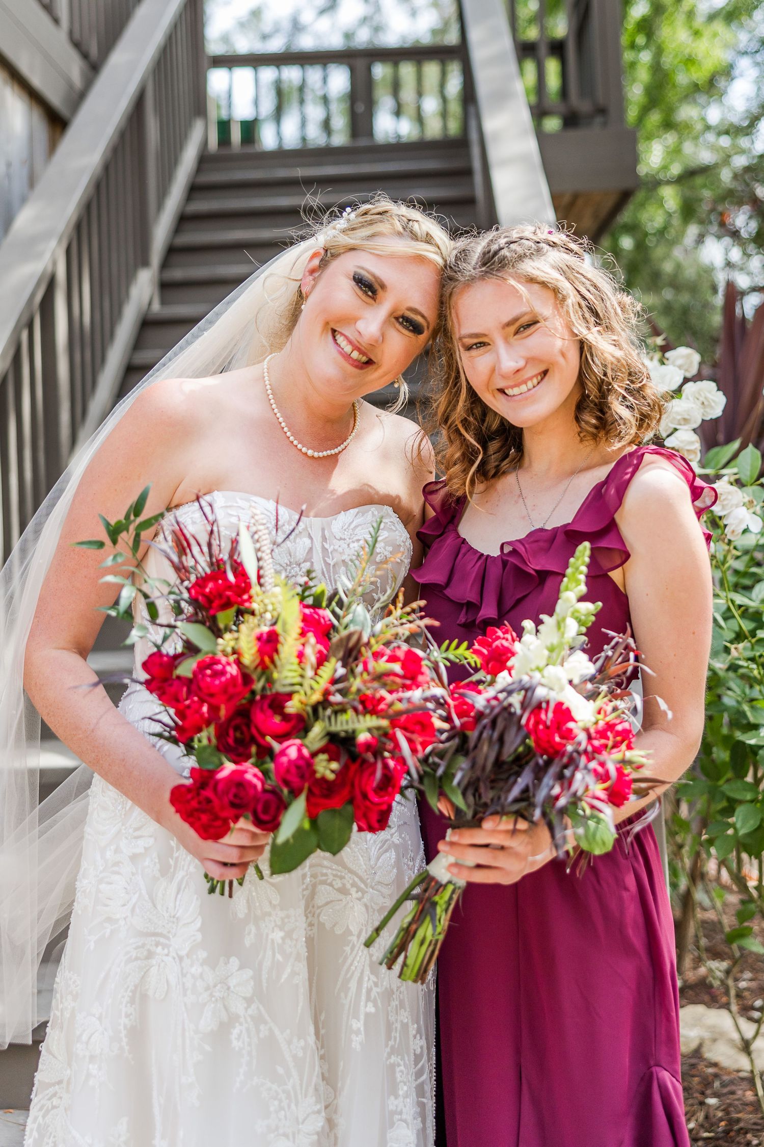 Two people share laughter while holding beautiful red and white floral bouquets on outdoor stairs.