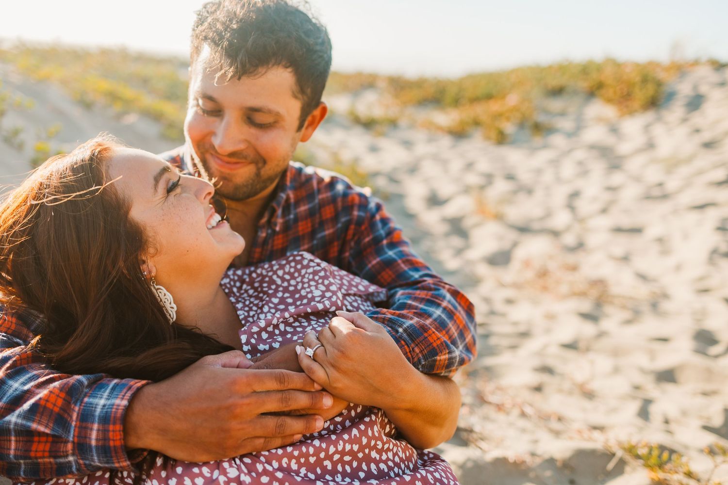 Joyful couple laughing together during beach photoshoot at sunset.