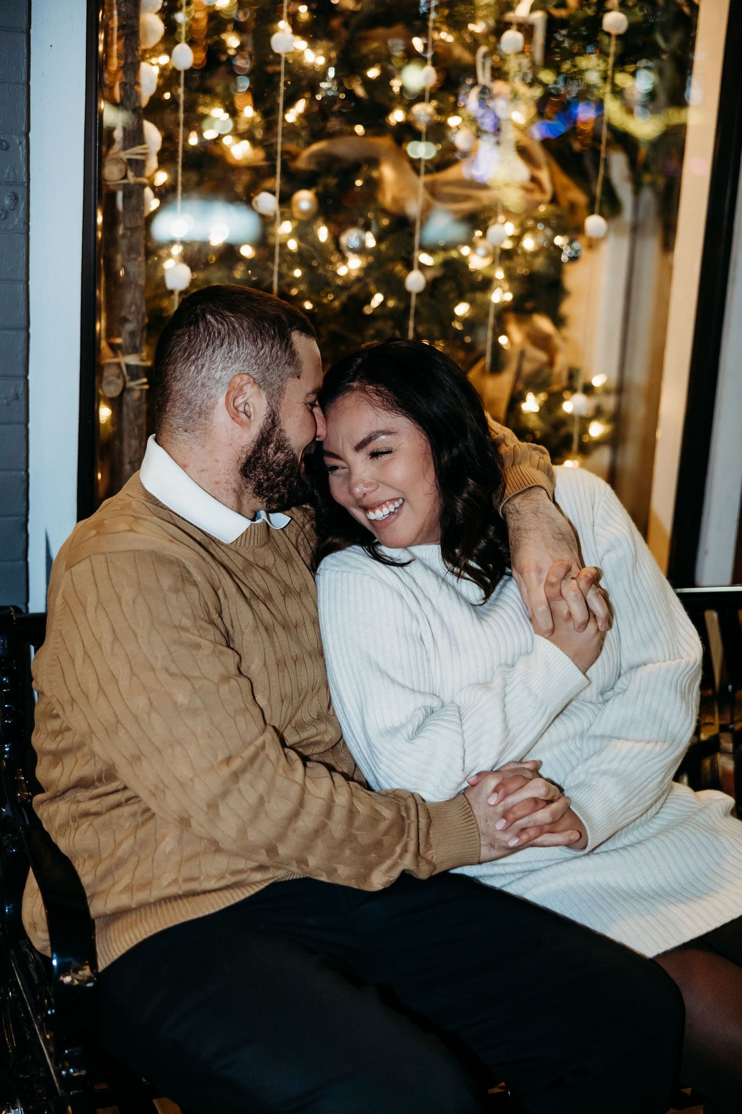 A couple shares an intimate moment on a couch with twinkling lights in the background.