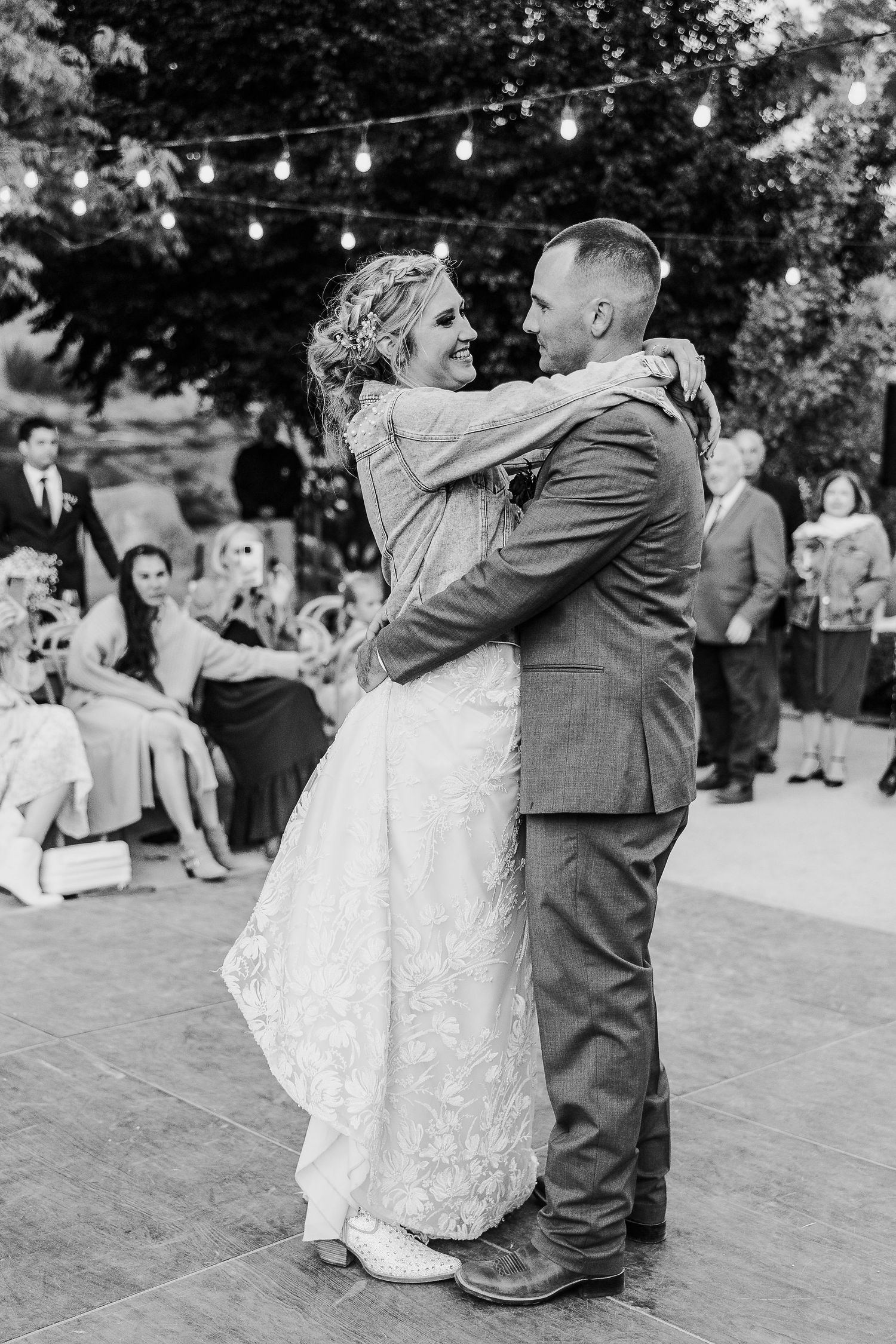 Black and white capture of newlyweds embracing during first dance at outdoor celebration.