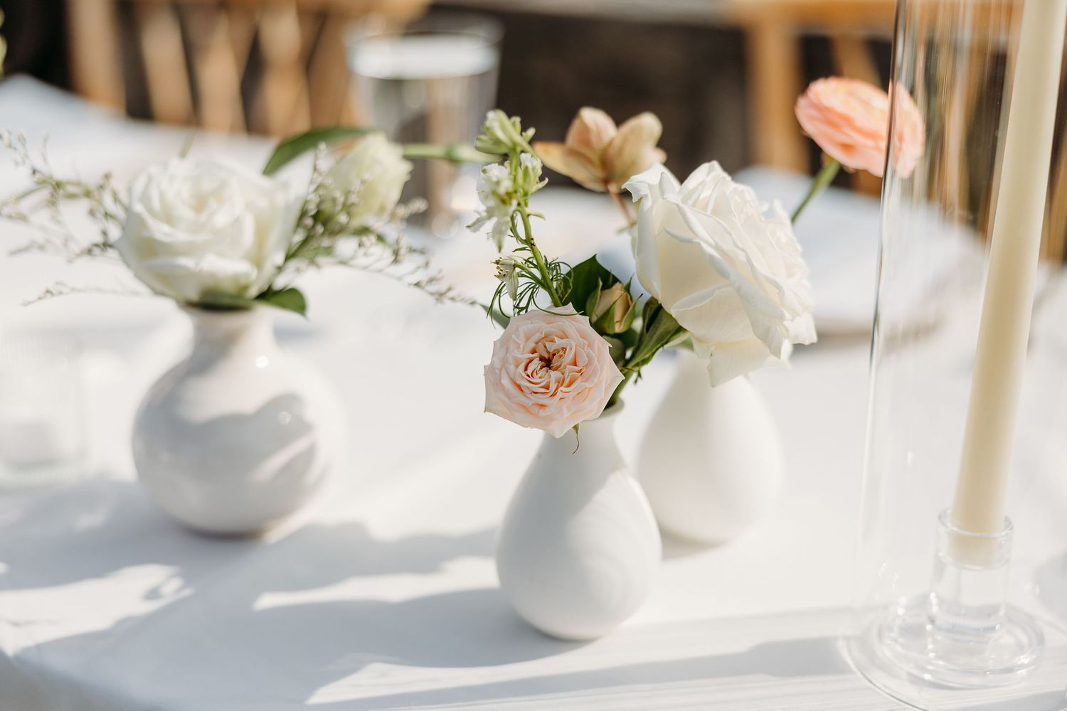 White bud vases with delicate pink and cream flowers create an elegant table centerpiece arrangement.