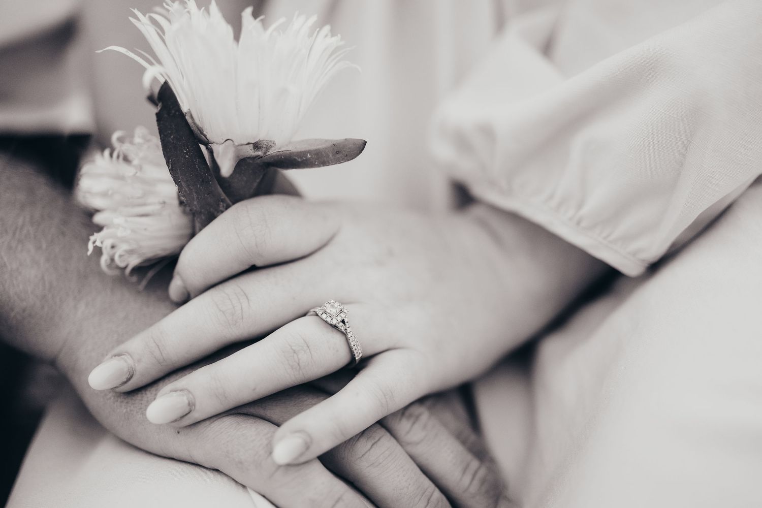 Close-up of engagement ring with white flower detail in black and white.