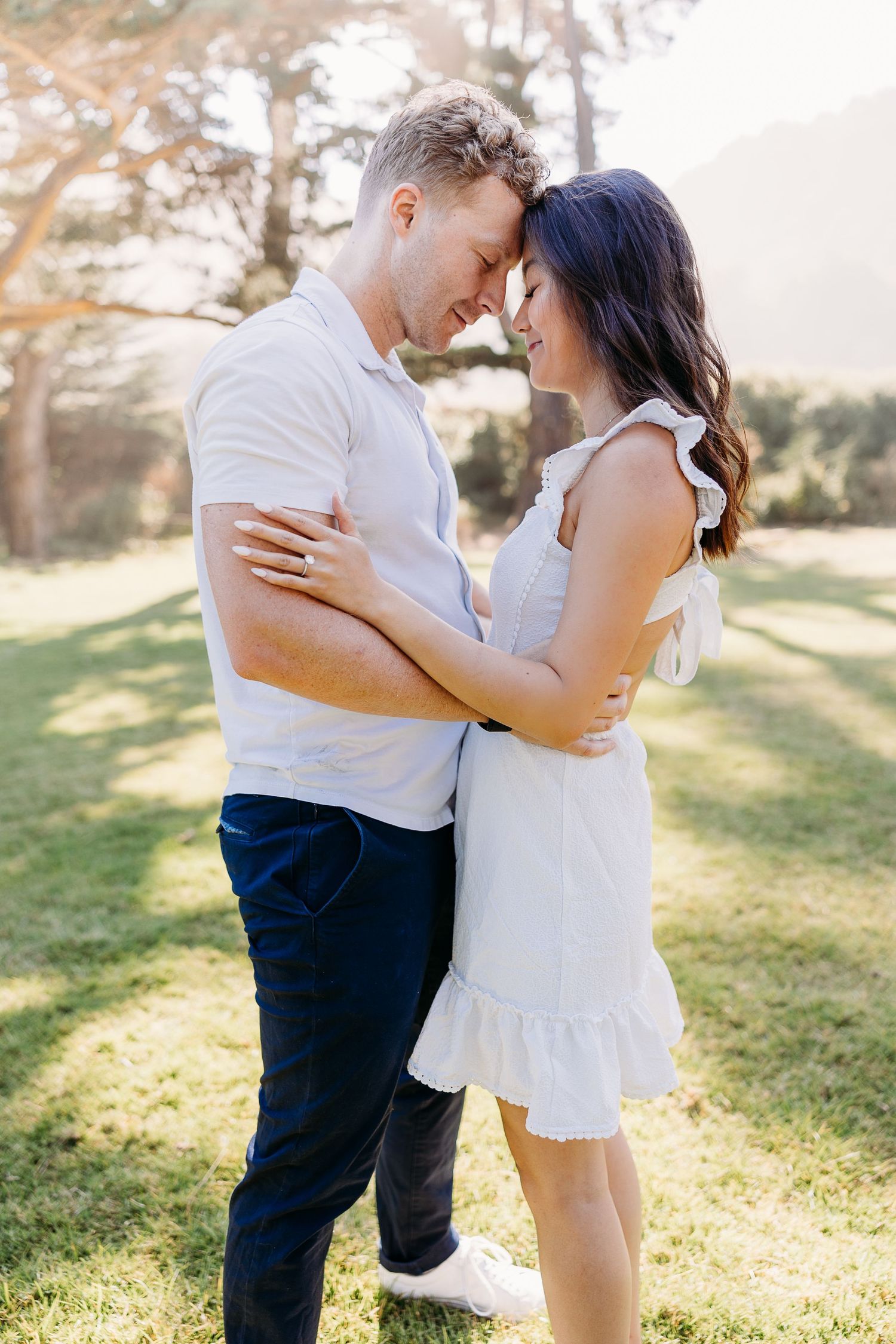 Couple in casual attire sharing a tender moment on a grassy hillside.