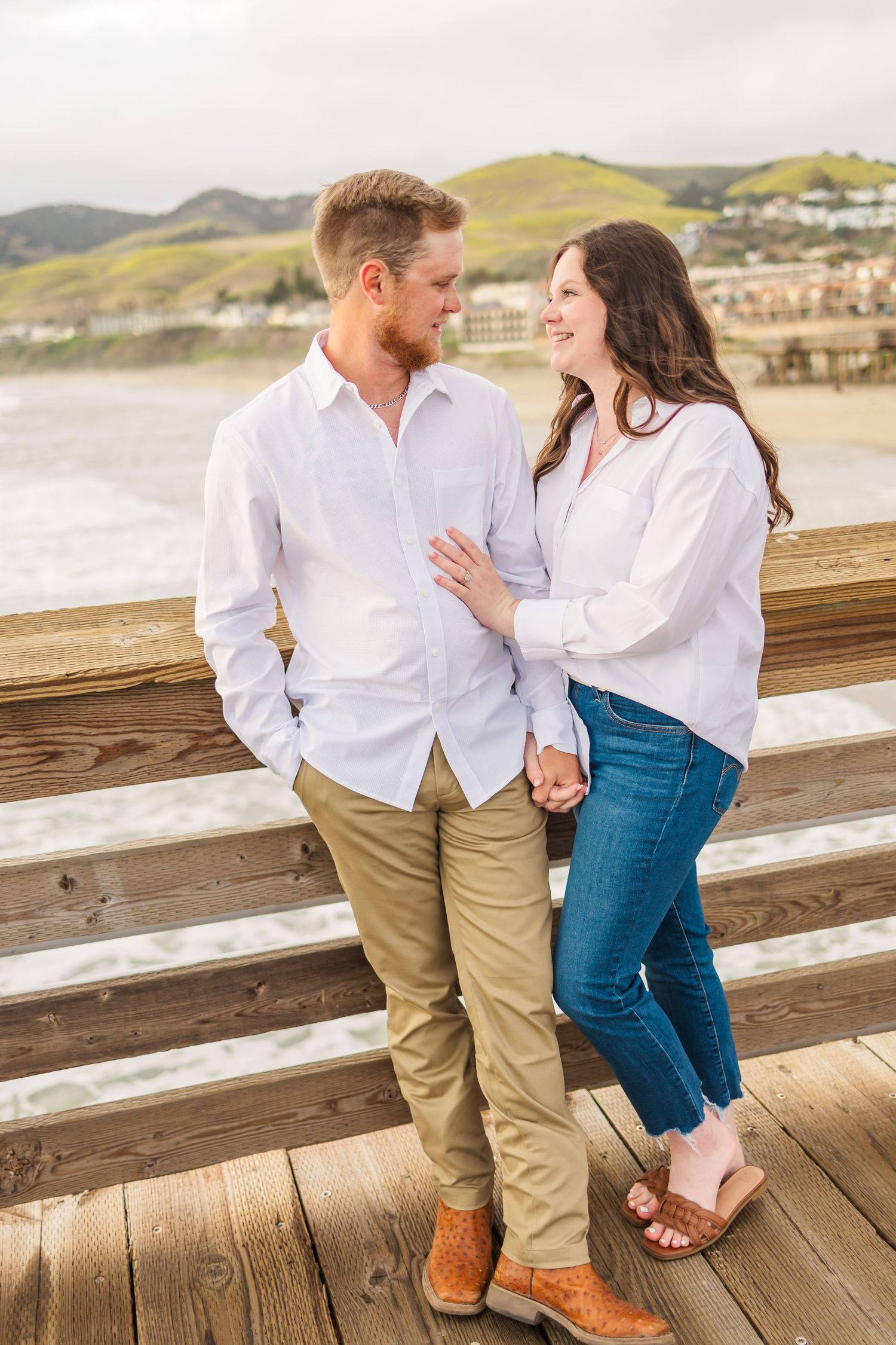 A couple in matching white shirts share romantic moment on oceanfront pier.