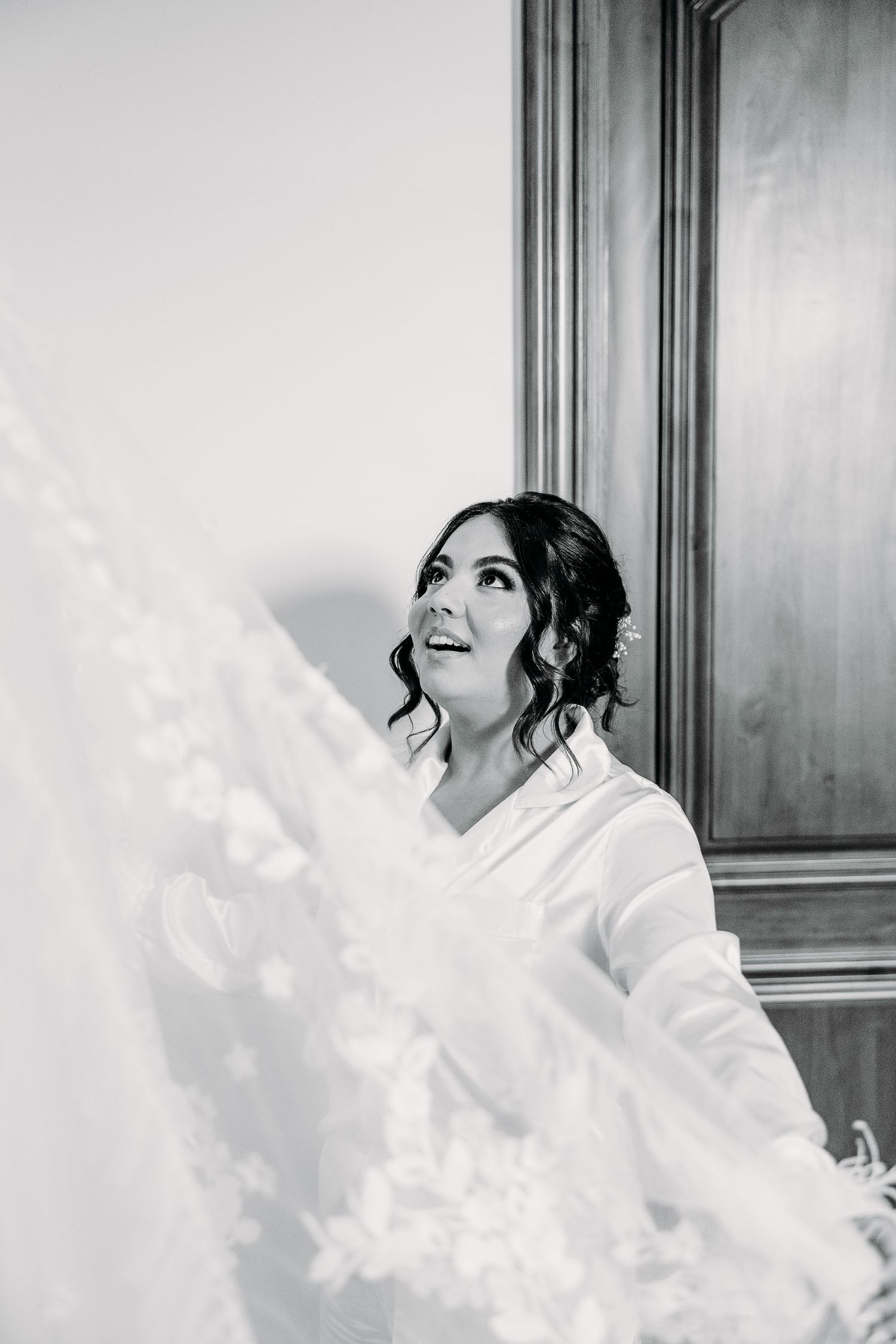 Black and white photo of someone admiring a flowing wedding veil against an elegant wooden panel background.