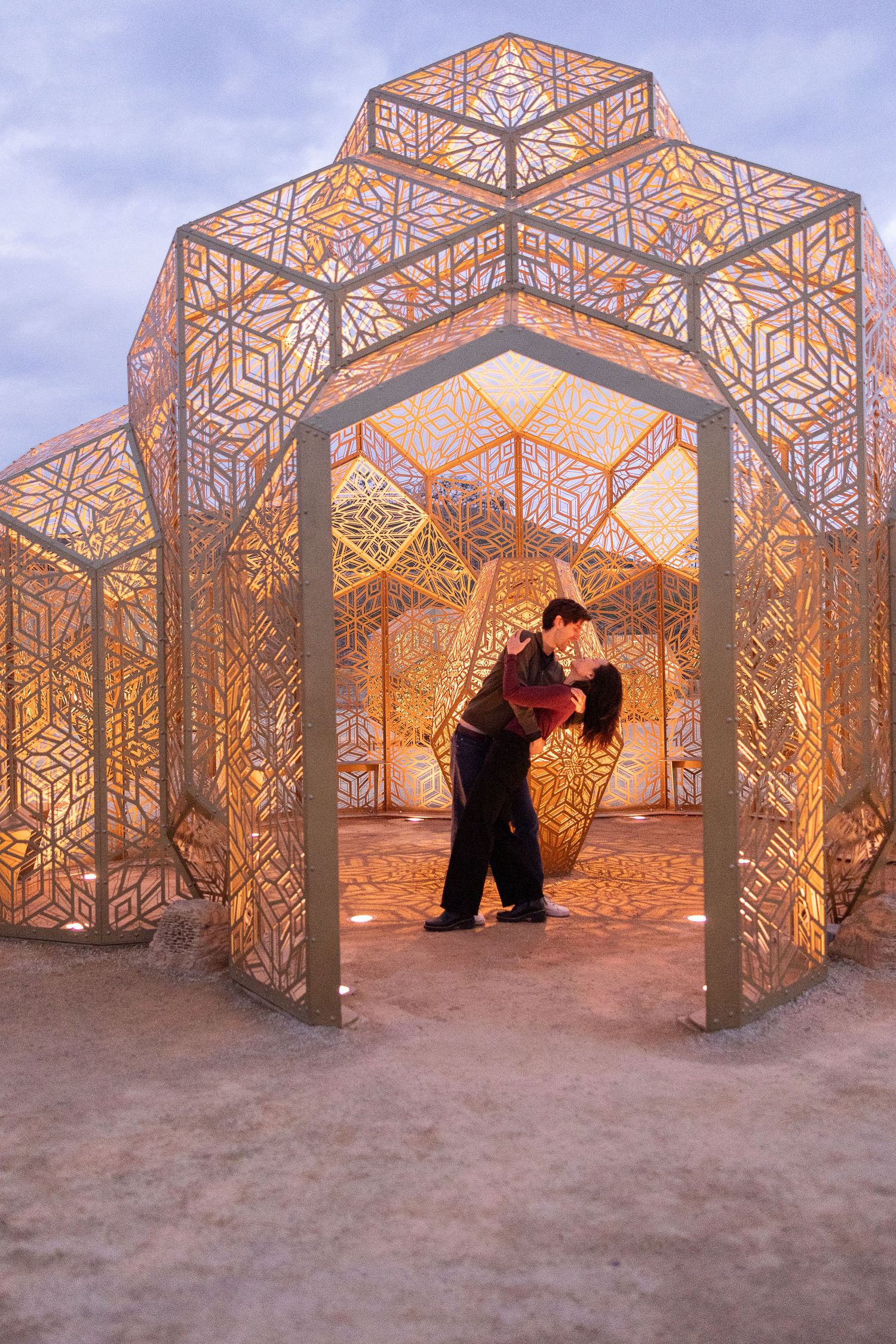 Ornate geometric metal panels create a maze-like art installation glowing at sunset in the desert.