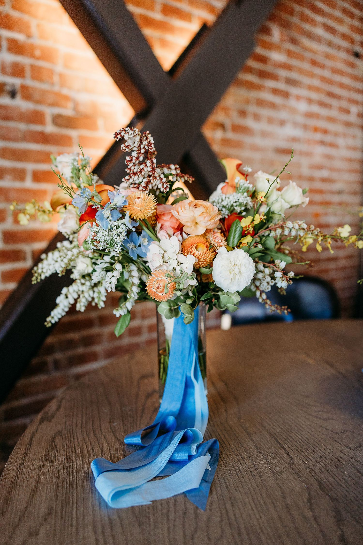 A beautiful floral arrangement with peach and blue blooms in a vase with flowing blue ribbons.