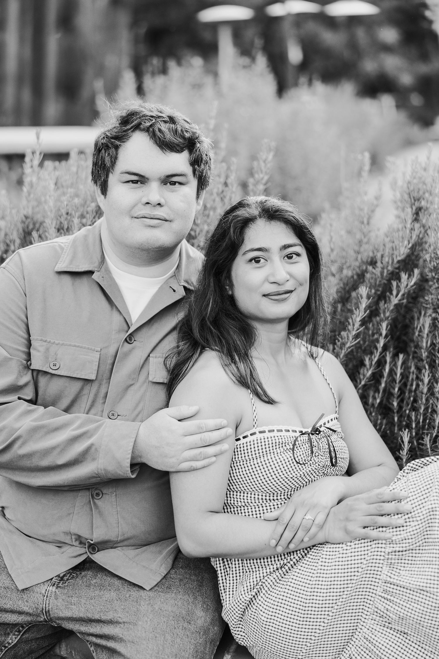 A couple sits together in a field of lavender for their engagement photos shot in black and white.