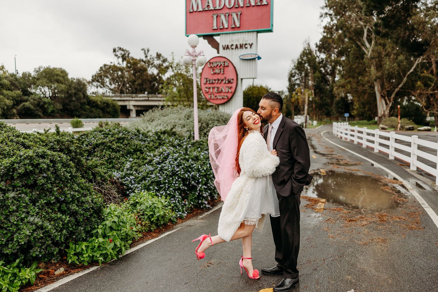 Couple dressed in vintage-inspired wedding attire posing together by a rustic red and white diner sign.
