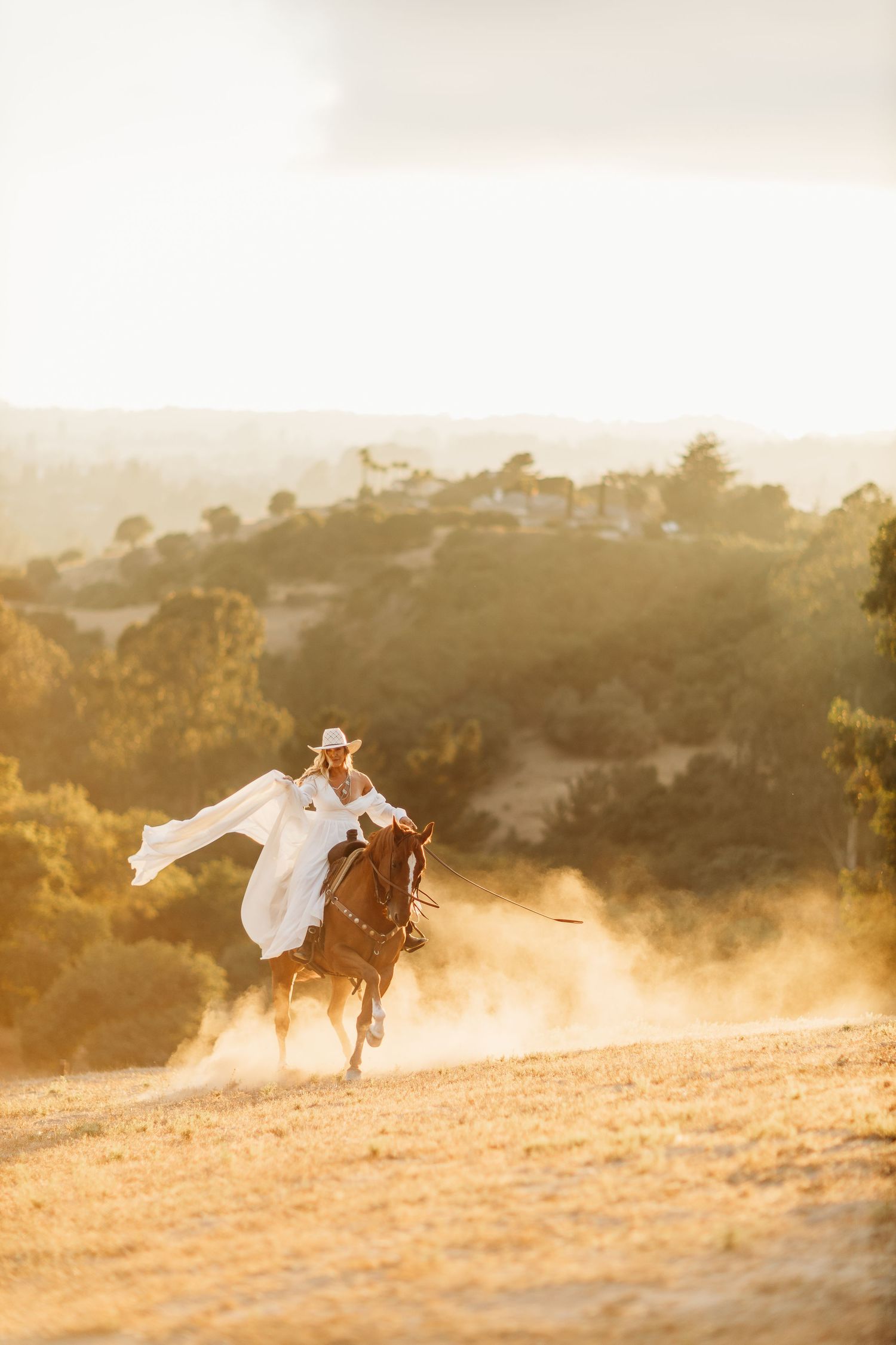 A white-clad rider gallops through golden sunlight on a mountain trail.