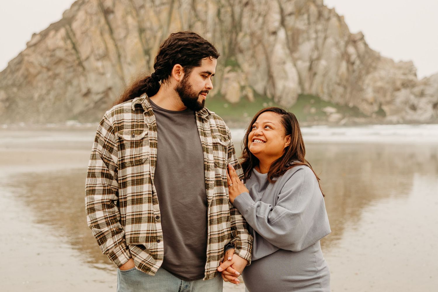 A couple shares a loving moment together on the beach with Morro Rock in the background.