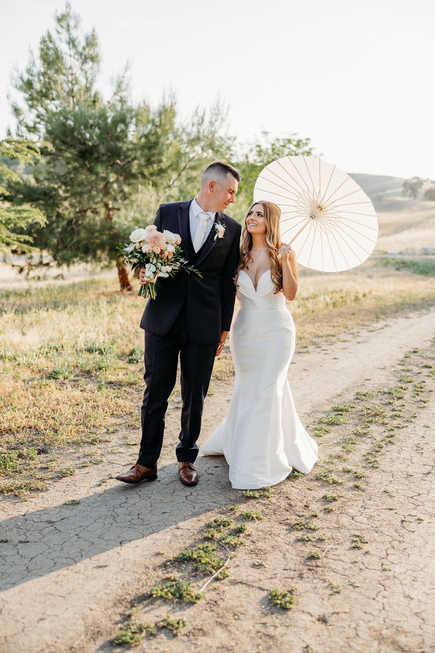 A romantic couple shares tender moments on a hillside path while holding a decorative white paper parasol.