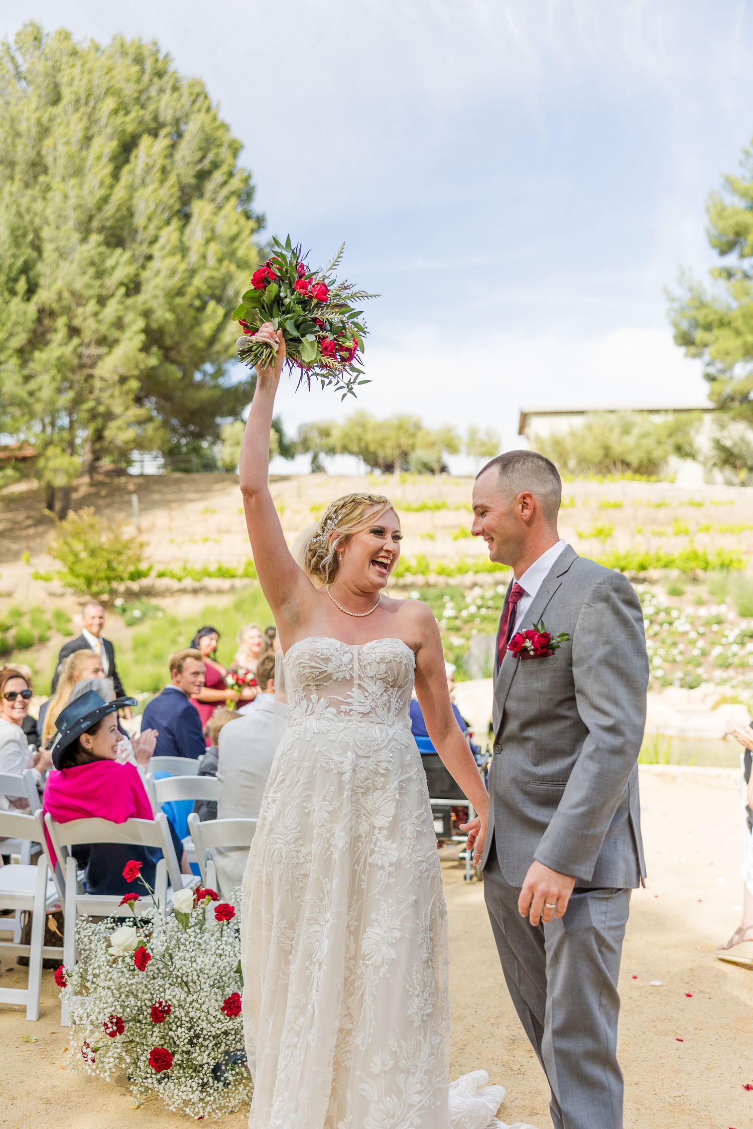 Celebratory moment at outdoor wedding with raised red bouquet.