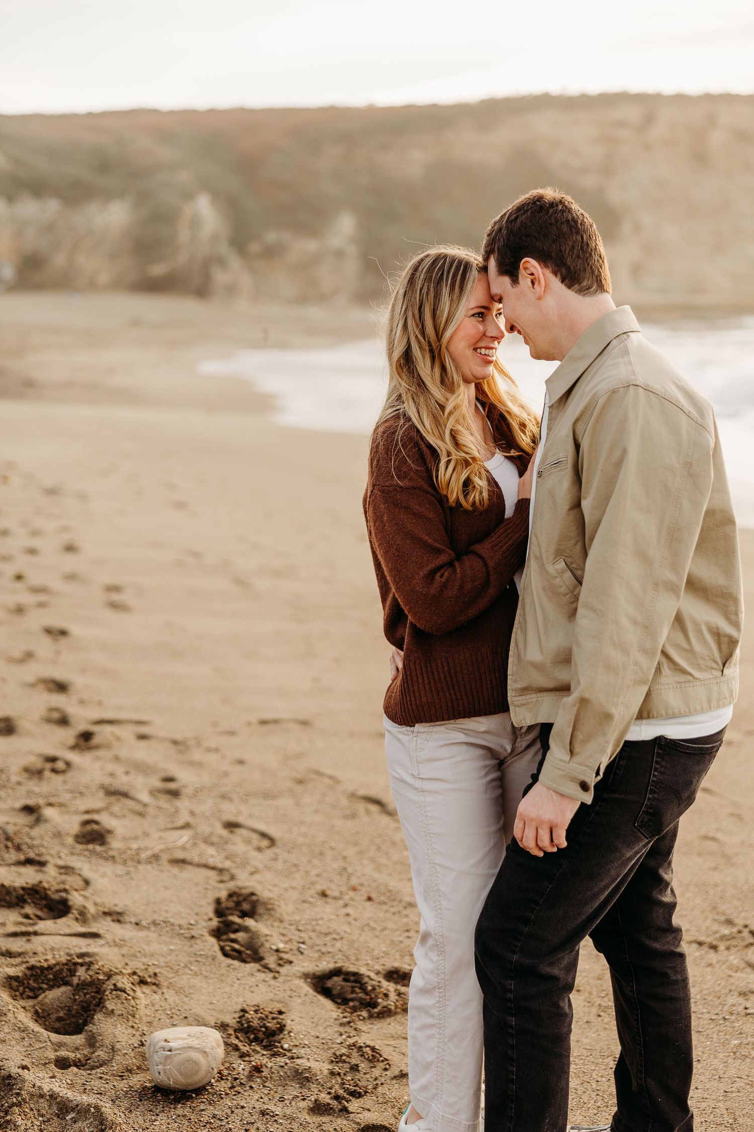 Intimate beach engagement photos with couple embracing on sandy shore at golden hour.