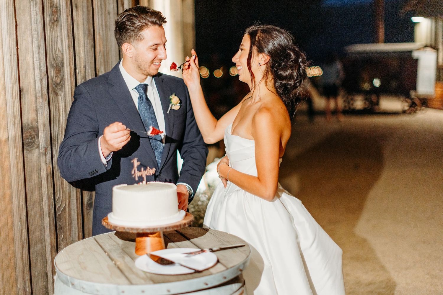 Wedding cake cutting scene with happy couple in rustic wooden venue setting.