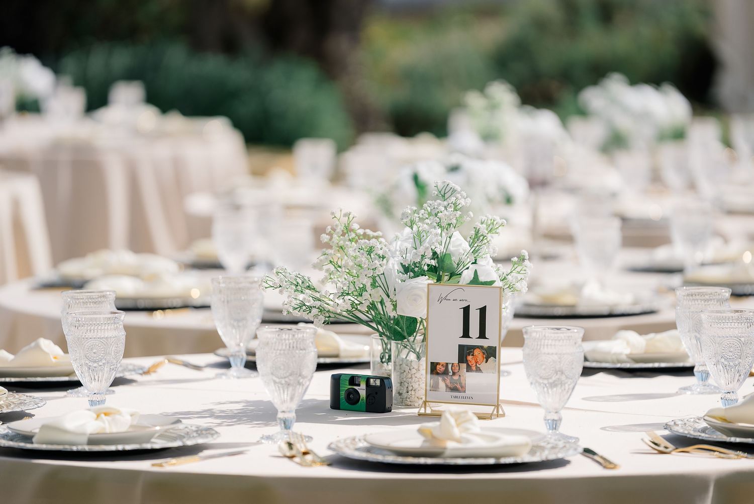 Elegant wedding reception table set with white florals, greenery centerpieces, and table number cards.