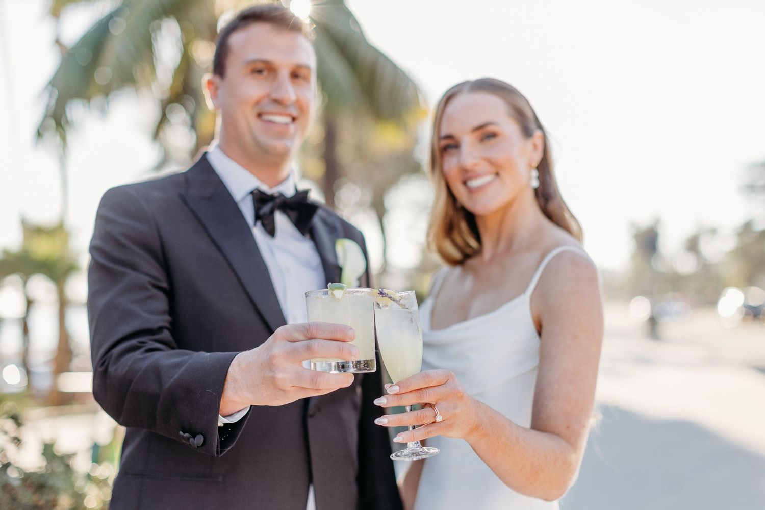 Wedding couple toasts with drinks at sunset celebration.