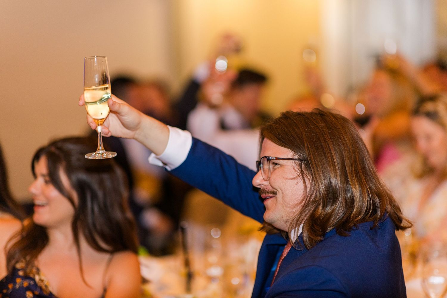 Wedding reception guests raising glasses during celebratory toasts at an elegant indoor venue.